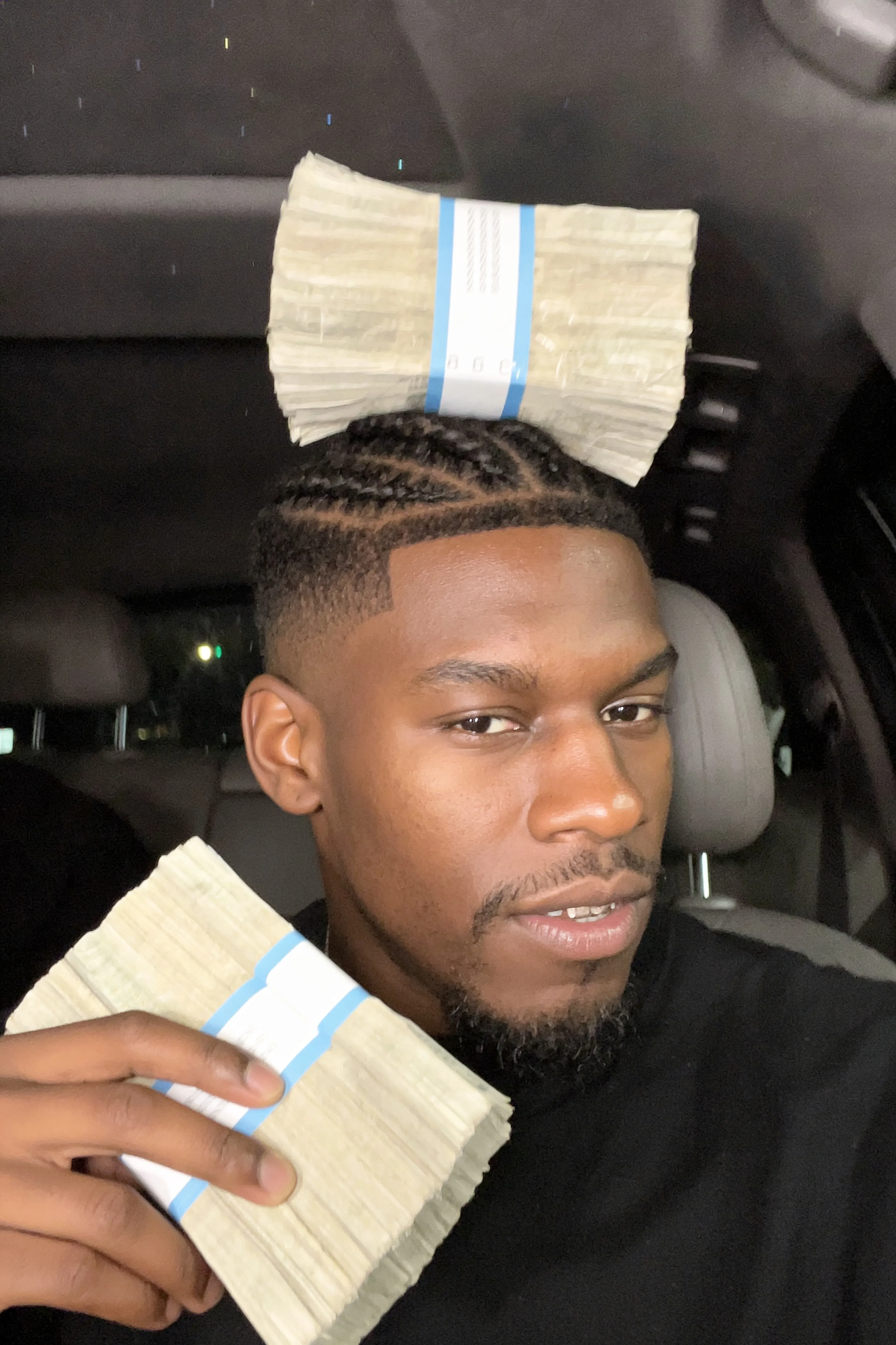 A person with a pixie cut and septum ring is holding stacks of money in a car.