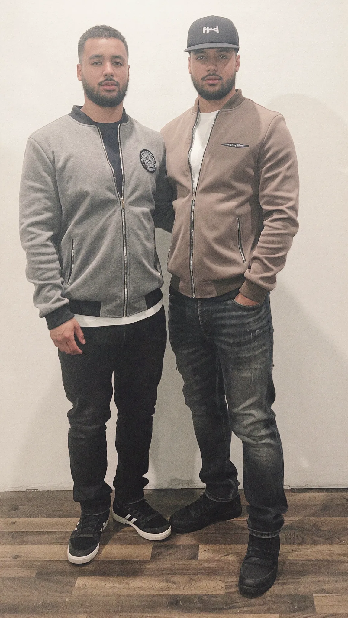 Two men stand side by side in a studio, dressed casually.