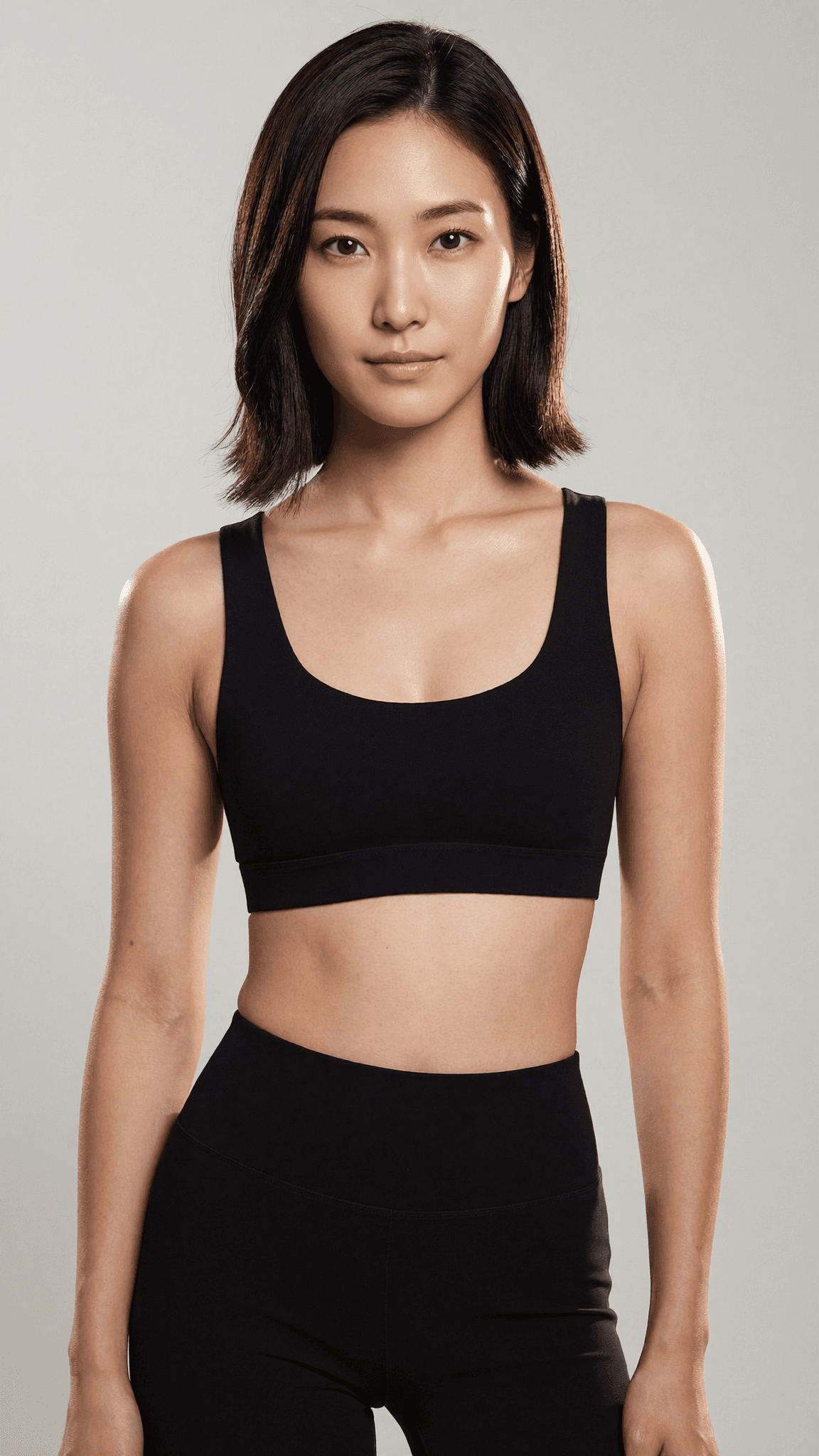 A woman in a black sports bra and leggings poses against a neutral background.