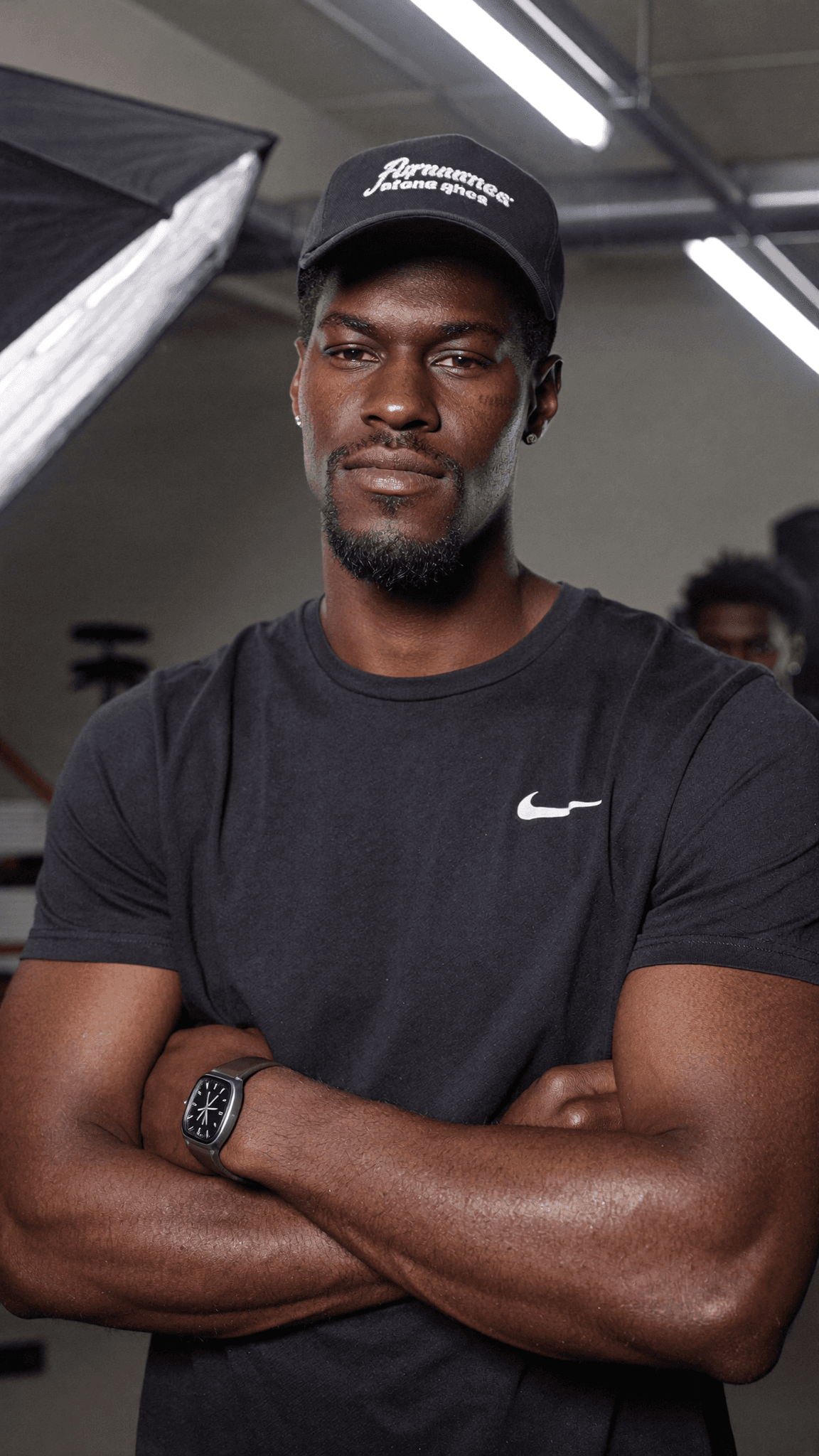 A man in a casual outfit stands confidently with arms crossed, wearing a cap and a Nike t-shirt.