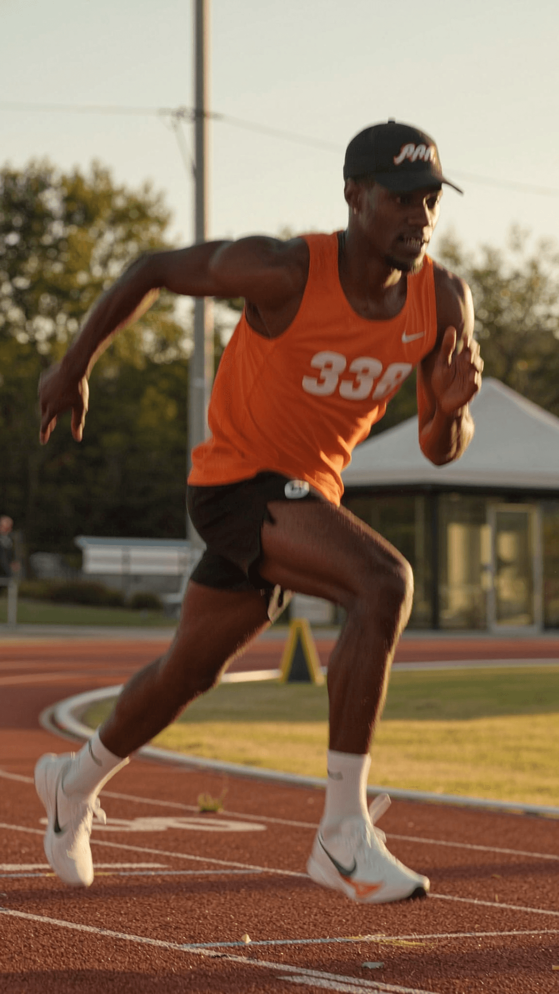 A person in an orange athletic outfit is running on a track during sunset.