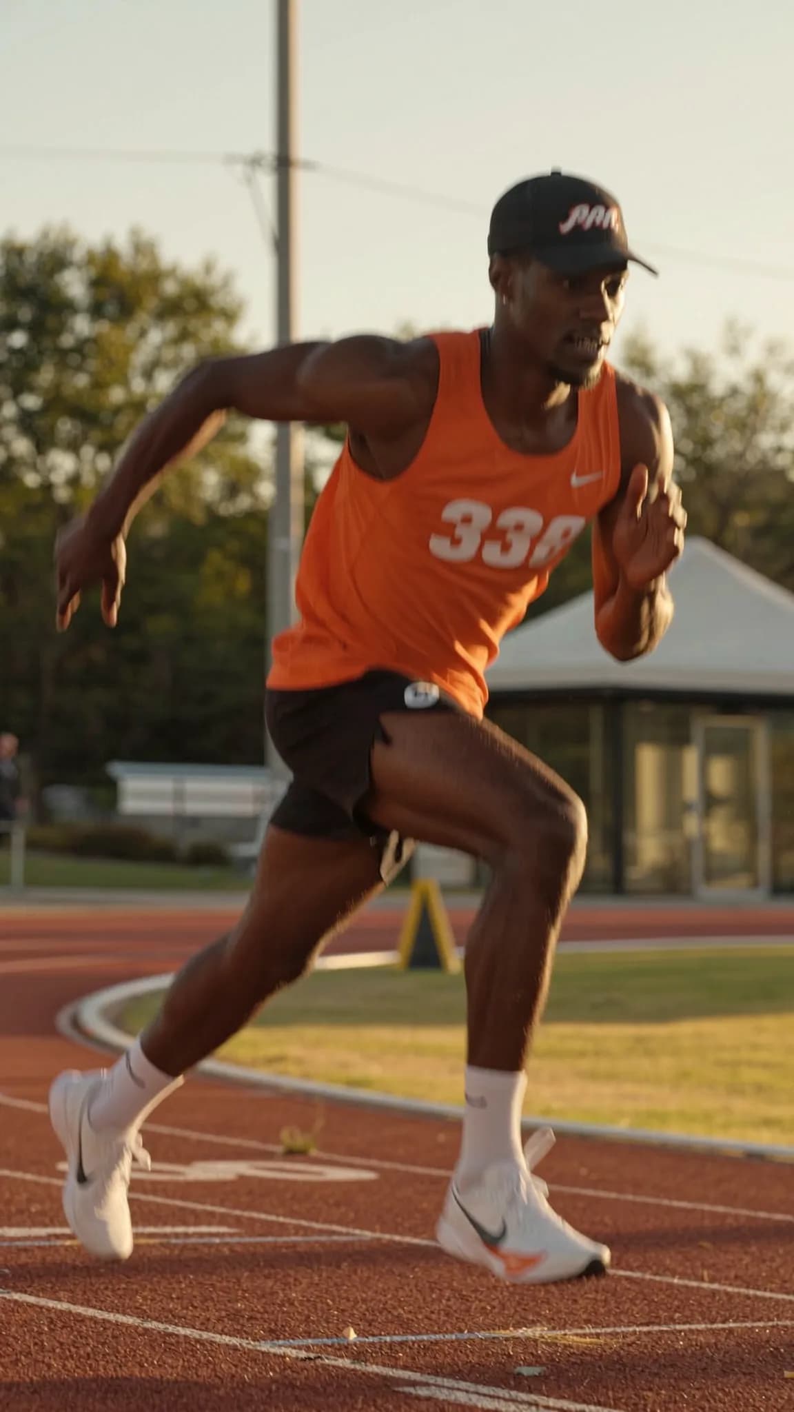 A person in an orange athletic outfit is running on a track during sunset.
