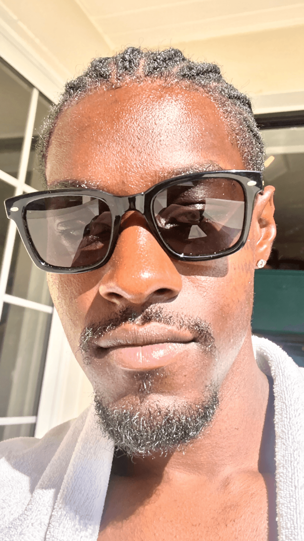 A person with a pixie cut and septum ring is wearing sunglasses outdoors in casual attire.