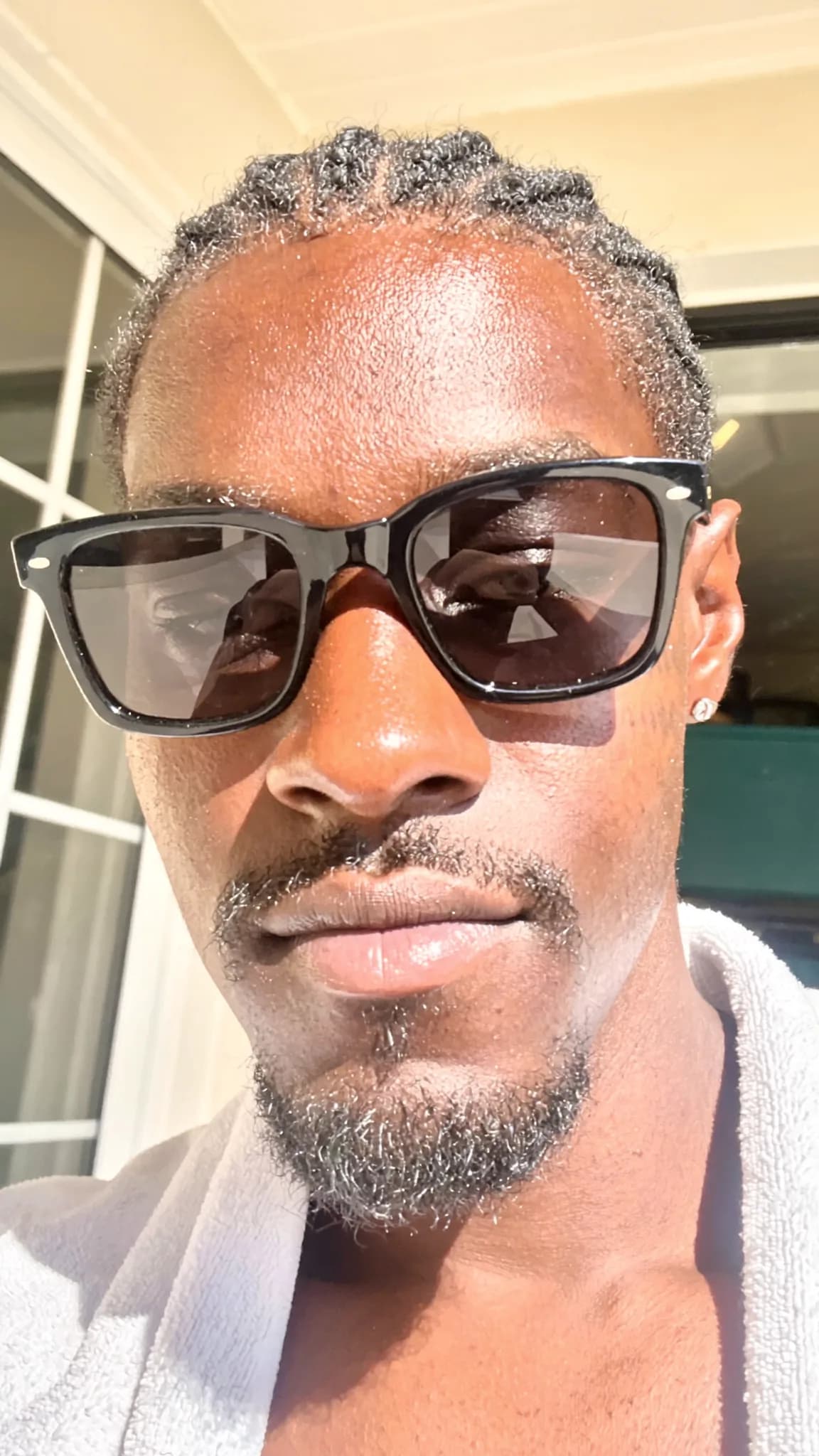A person with a pixie cut and septum ring is wearing sunglasses outdoors in casual attire.