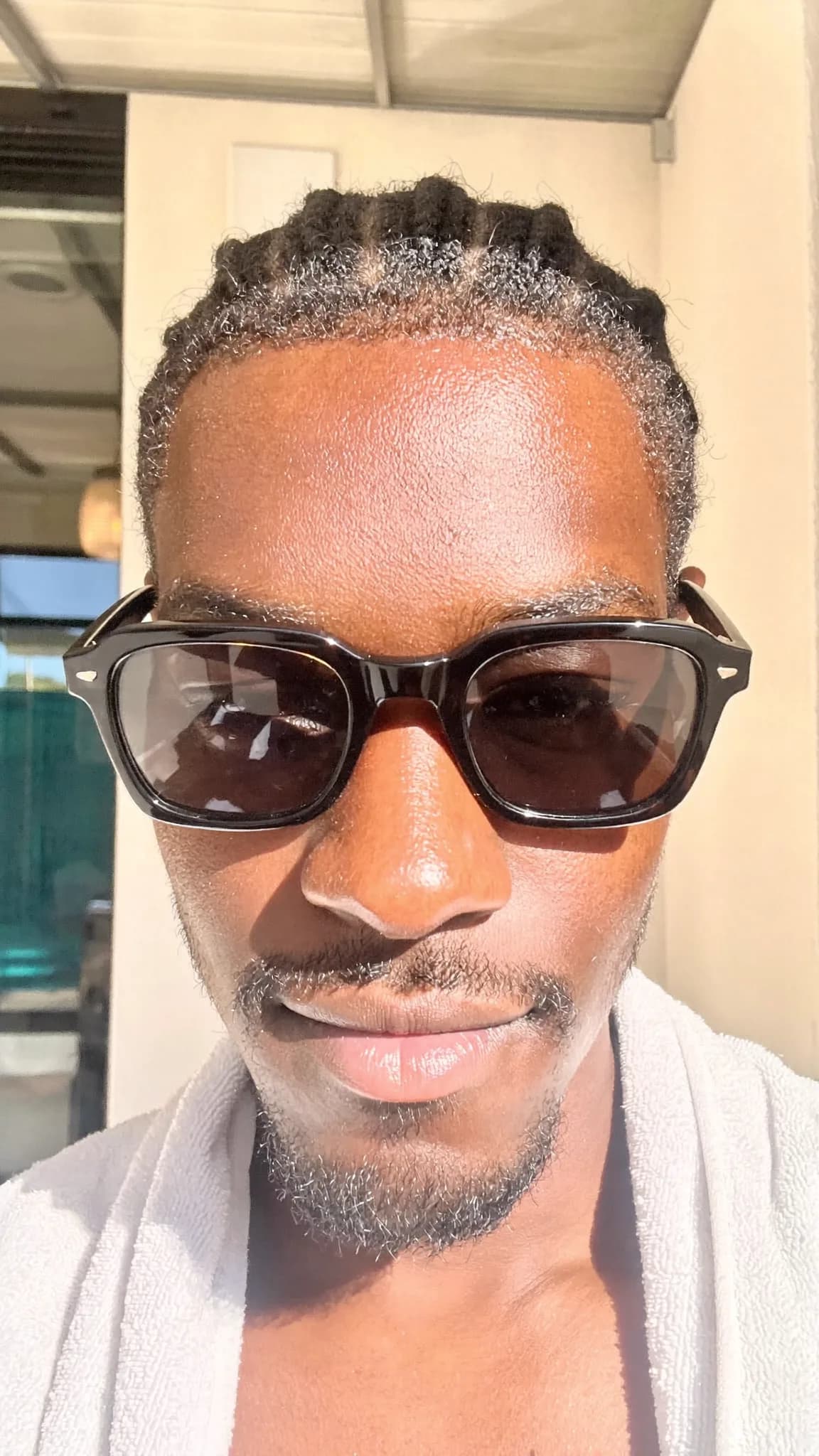 A person with a pixie cut and septum ring is wearing sunglasses and casual clothing, posing for the camera outdoors.