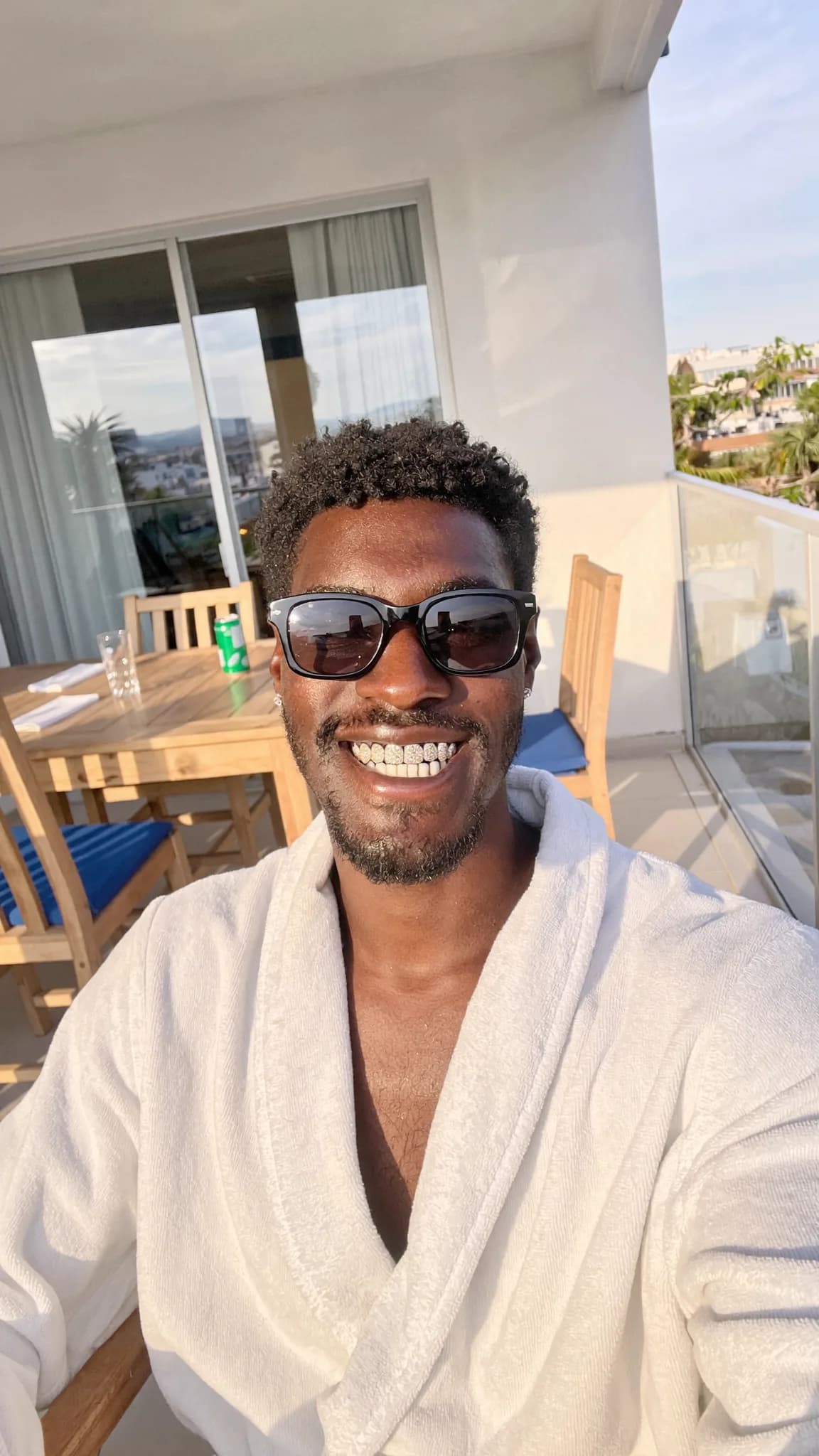 A person wearing a robe poses on a balcony with a relaxed and playful demeanor.