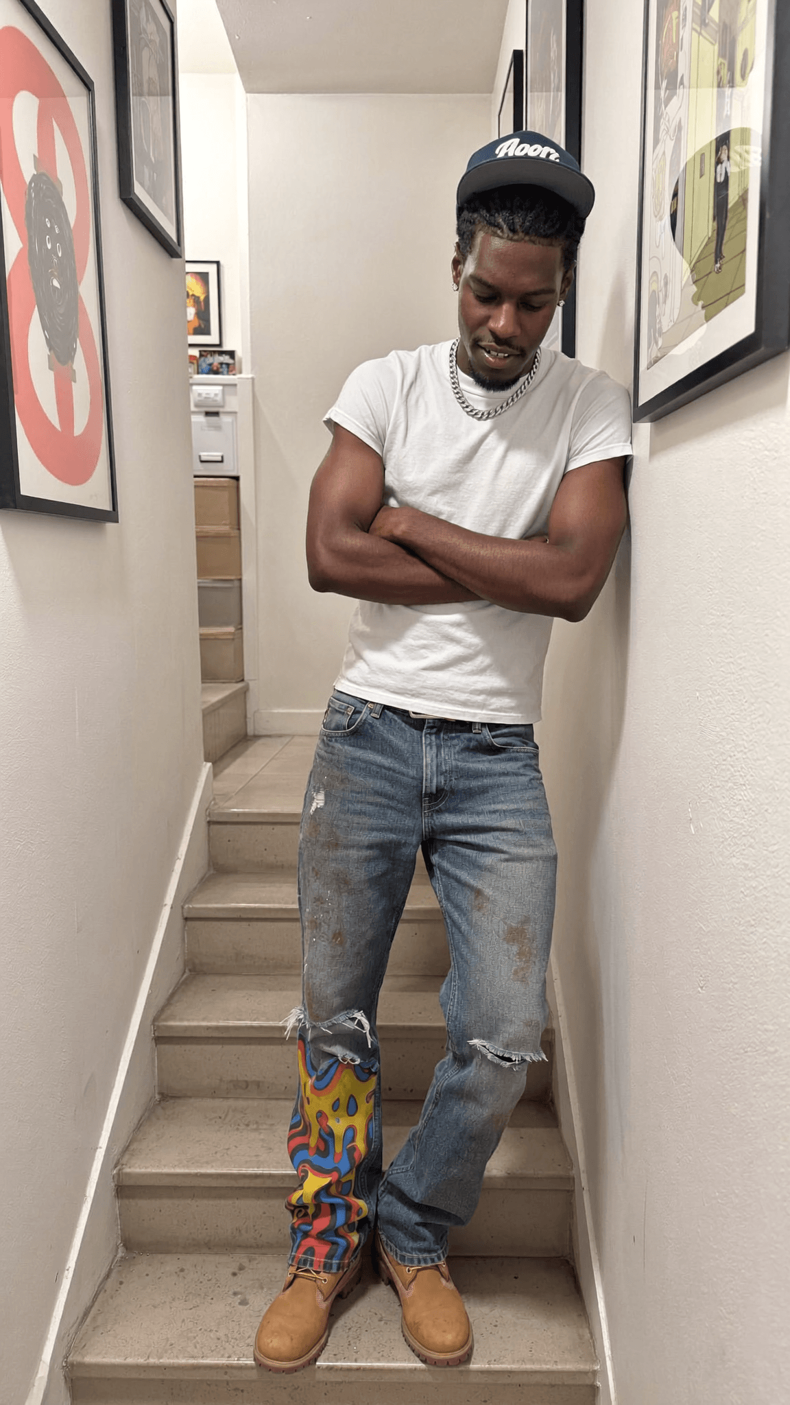 A person stands on stairs wearing casual clothing with a playful expression.