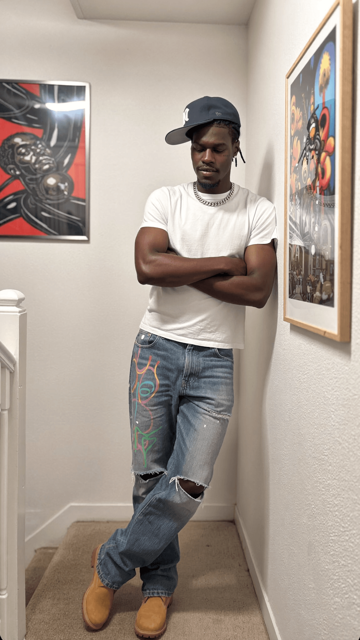 A person stands in a hallway with arms crossed, wearing casual clothing and posing for the camera.