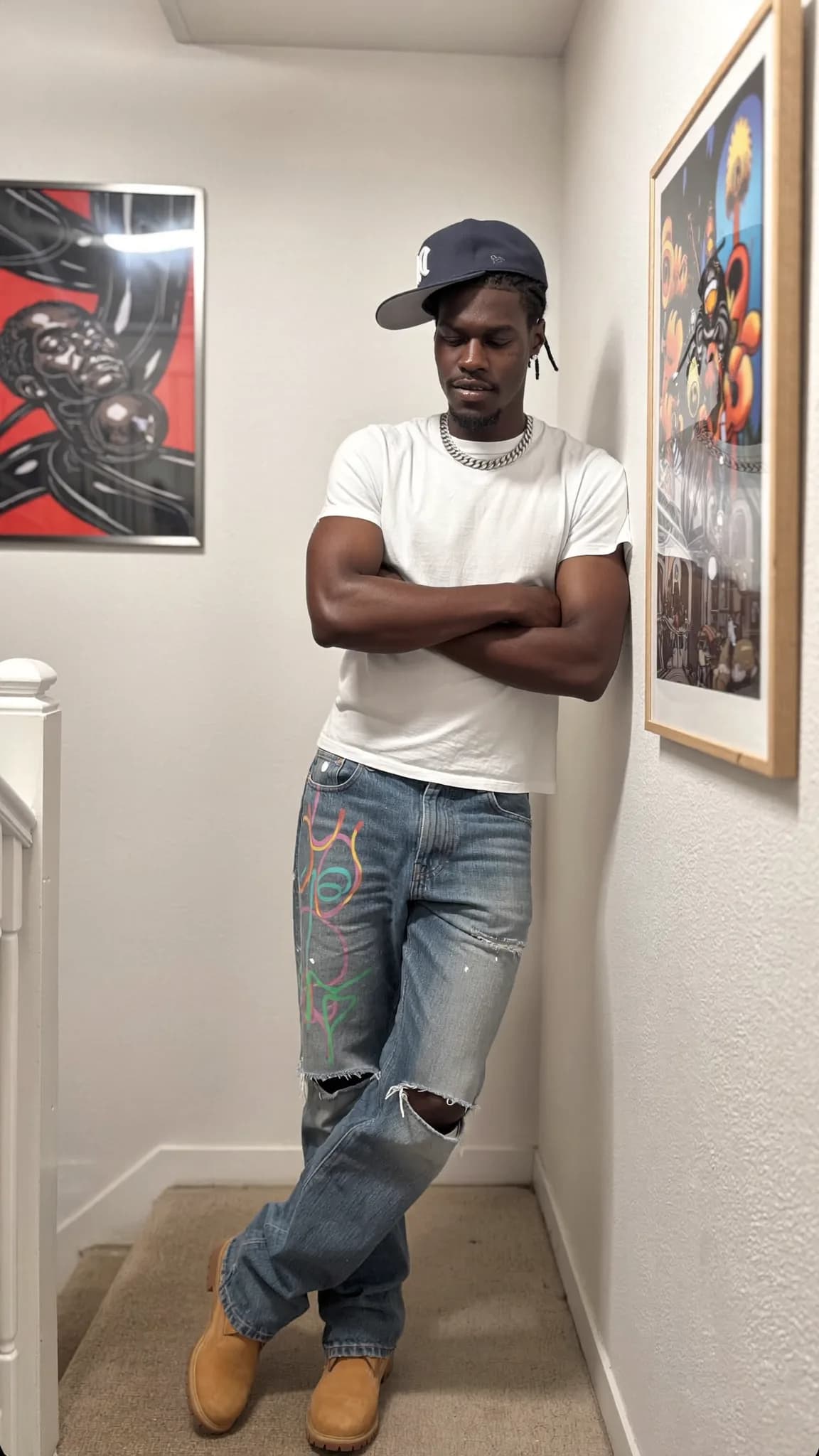 A person stands in a hallway with arms crossed, wearing casual clothing and posing for the camera.