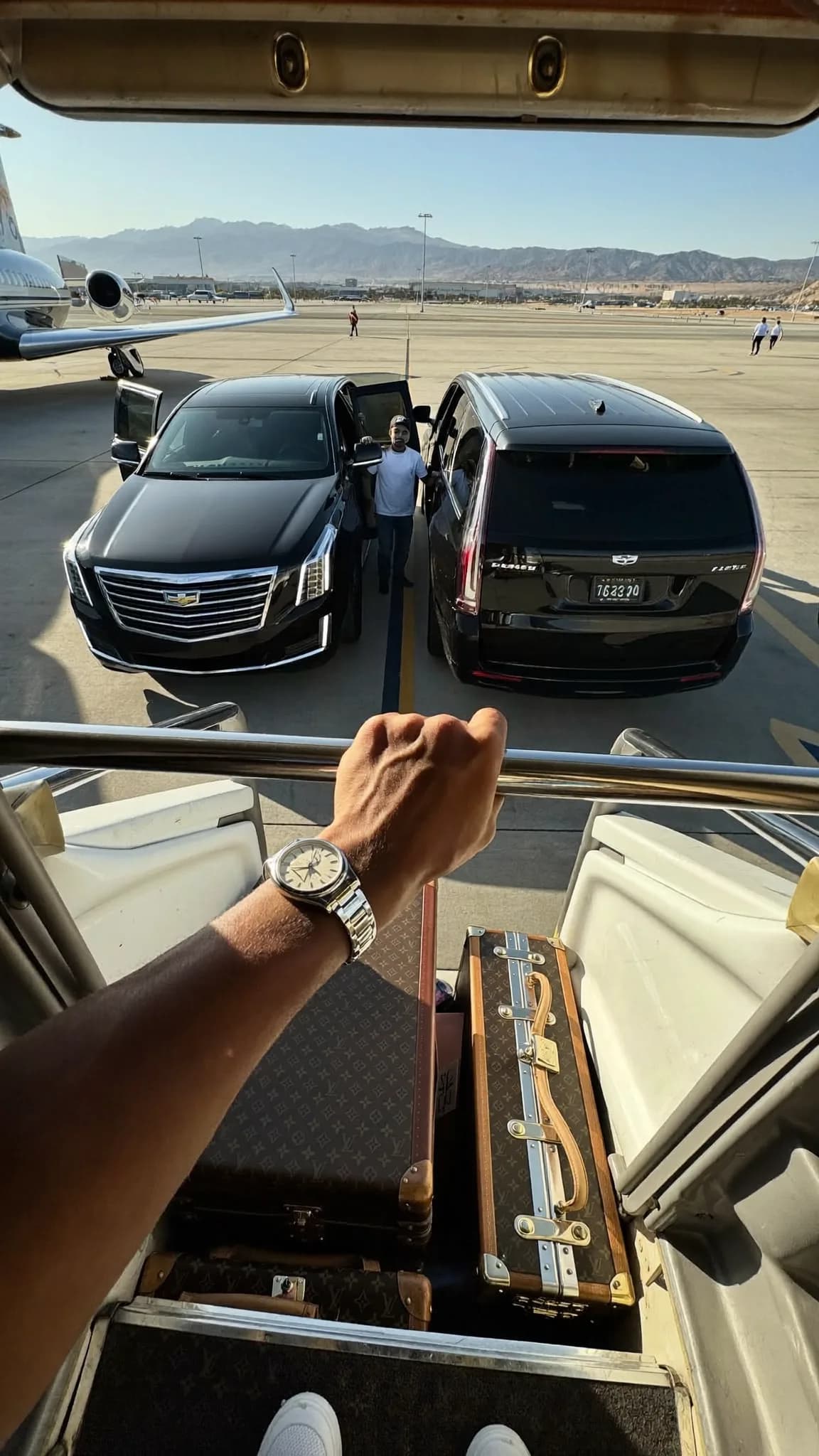 A person stands at the entrance of a luxury vehicle, holding open the door for another individual.