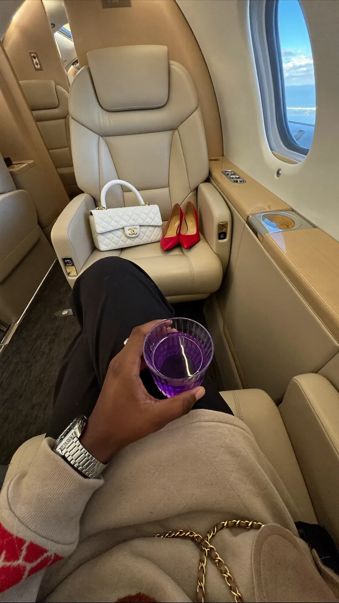 A person is seated in a luxurious setting, holding a purple drink and wearing casual attire.