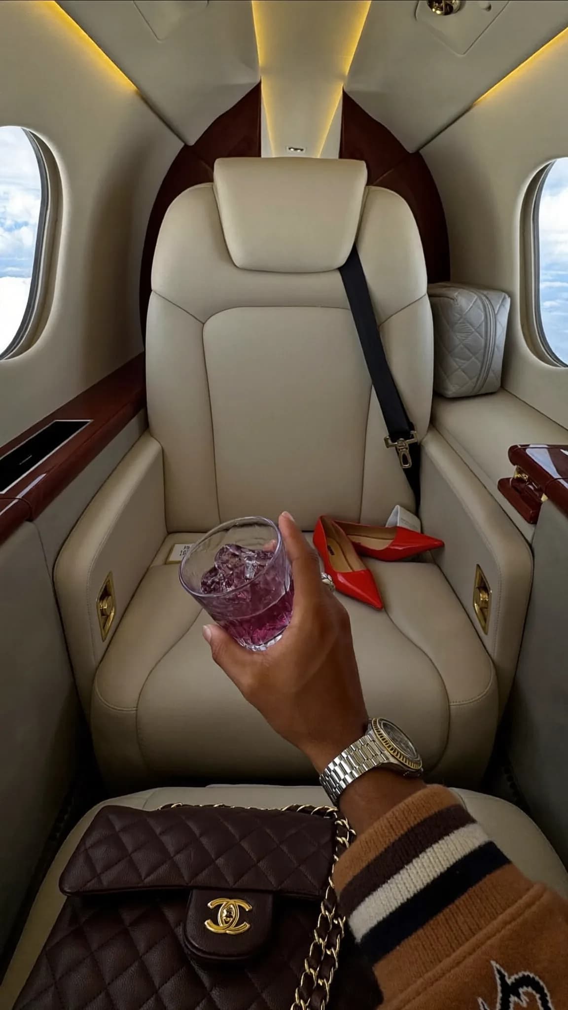 A person is seated in a luxury car, holding a drink and wearing casual attire.