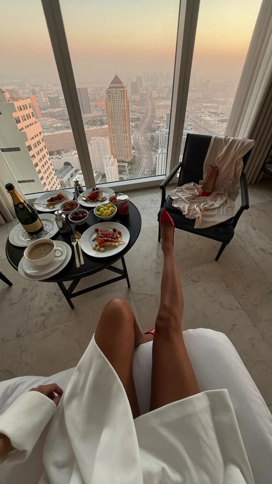 A woman enjoys a meal on a balcony with a city view, dressed casually and in a playful mood.