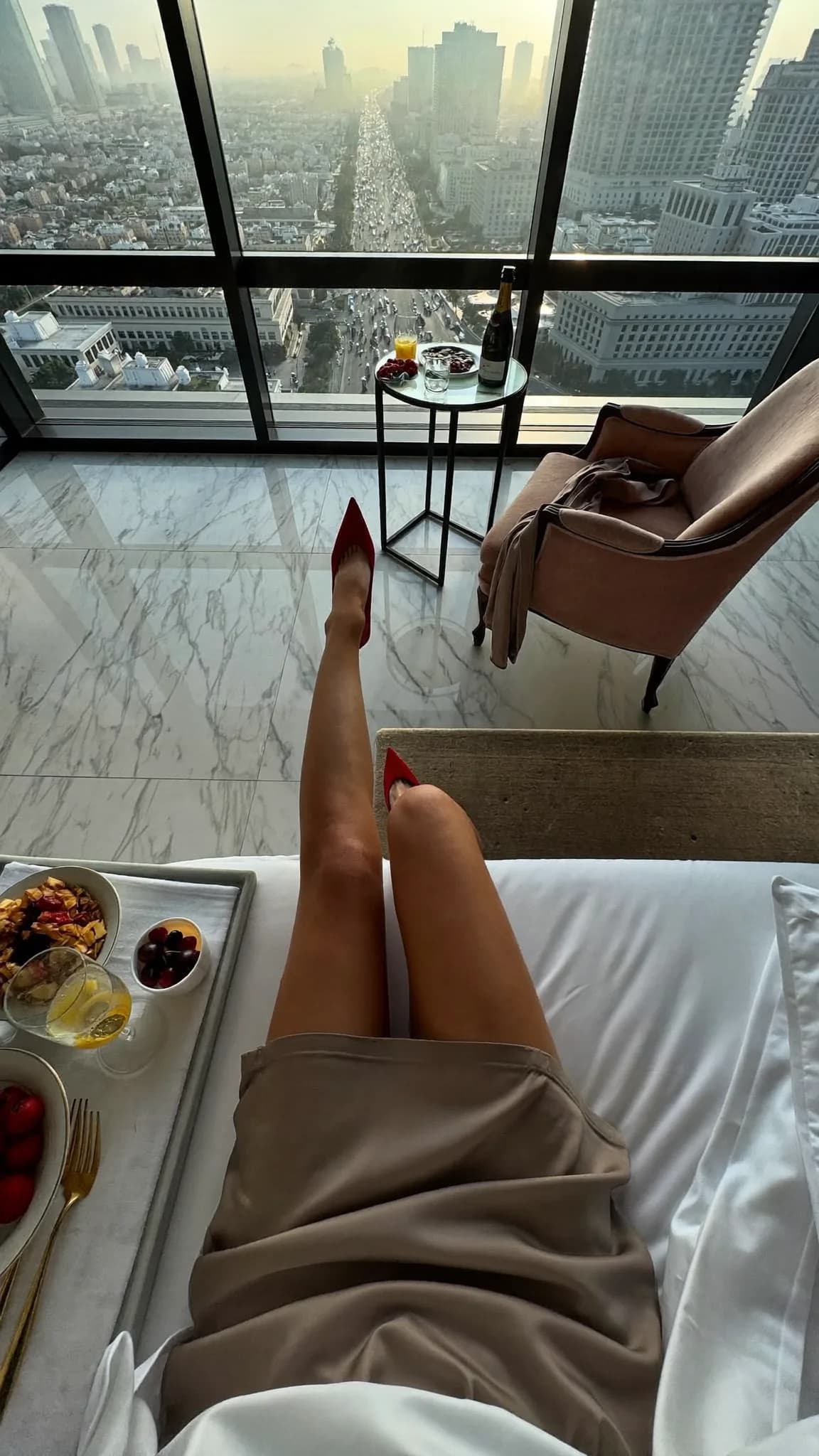 A person lounges on a balcony with a city view, enjoying breakfast in bed.