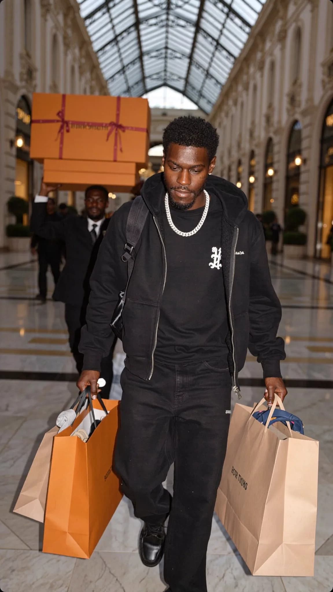 A man in casual attire is walking through a shopping mall carrying multiple bags.