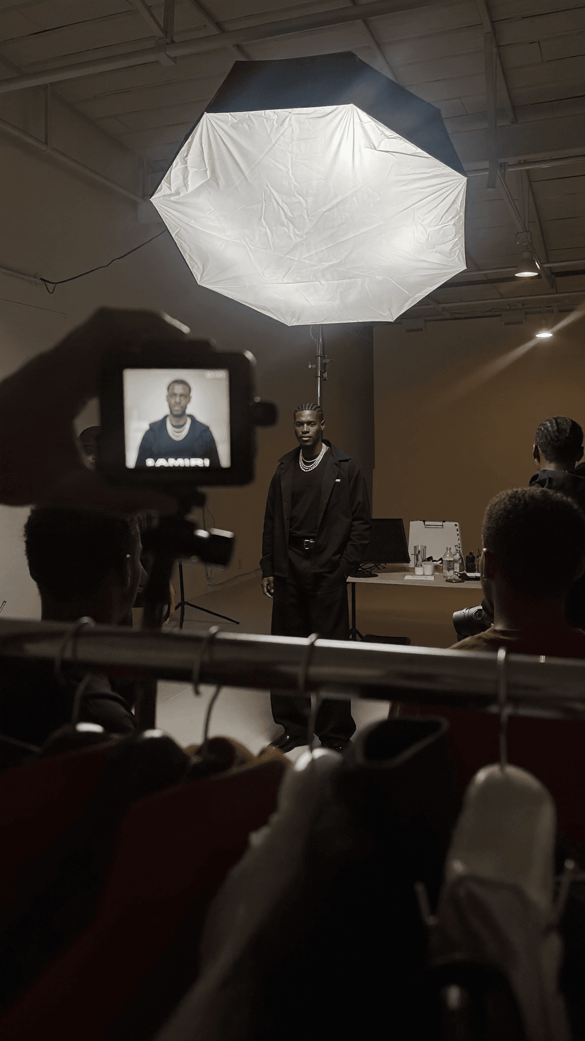 A person is being photographed in a studio setting with casual attire and soft lighting.