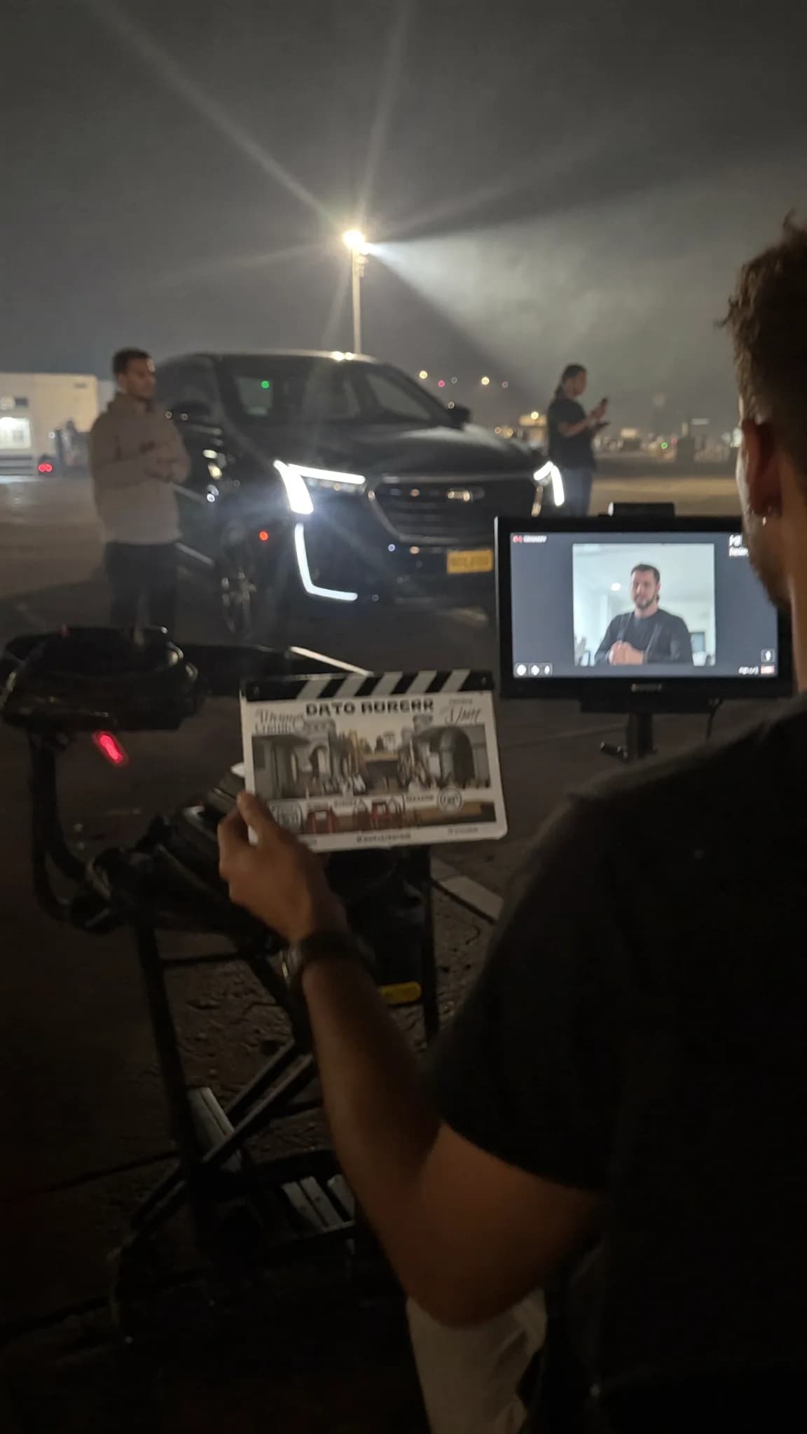 A person is filming a scene outdoors at night with a car in the background.