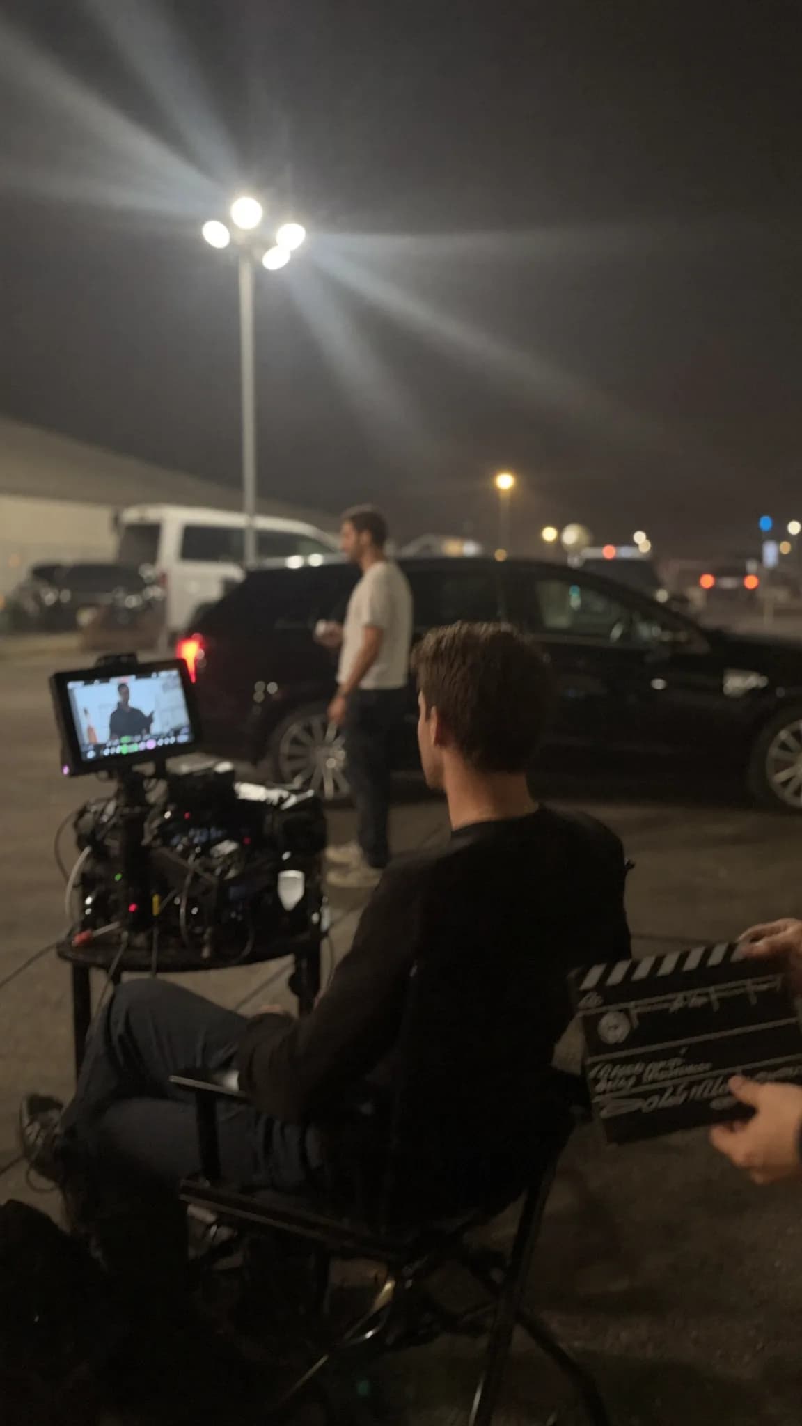 A film crew is working outdoors at night with a clapperboard in hand.