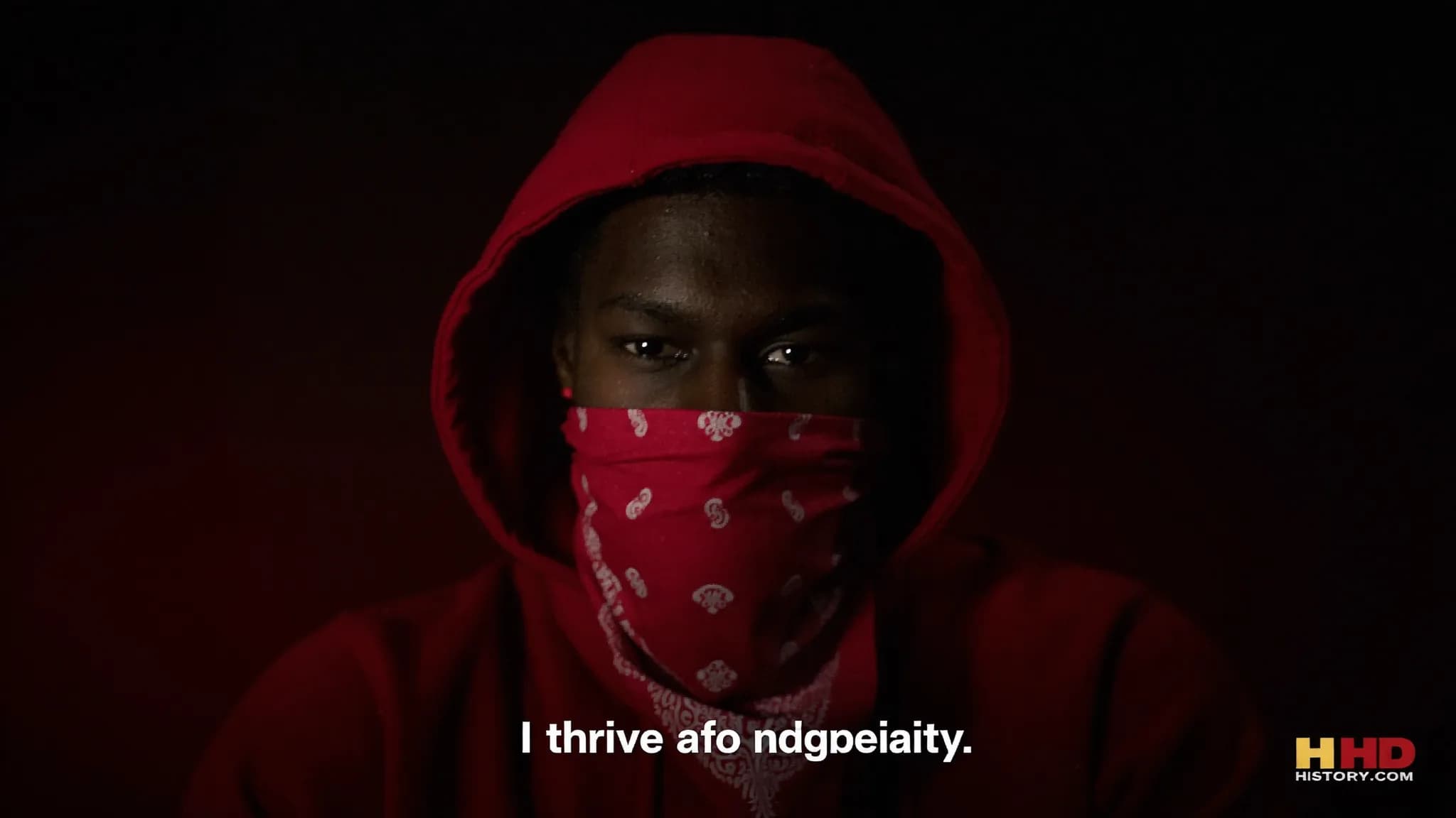 A person wearing a red hoodie and bandana poses in a studio setting.