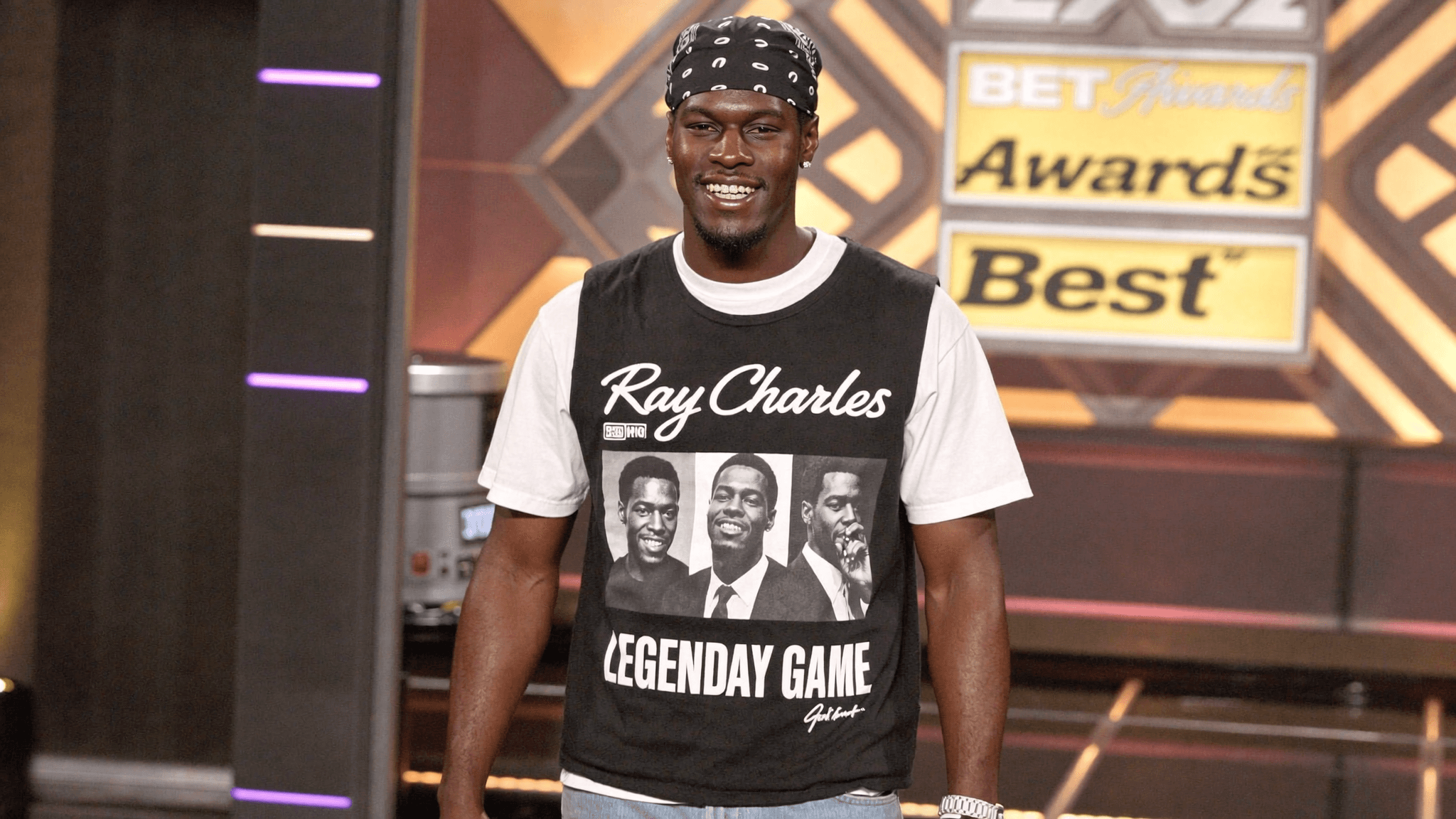 A man wearing a casual outfit stands in front of a BET Awards backdrop.