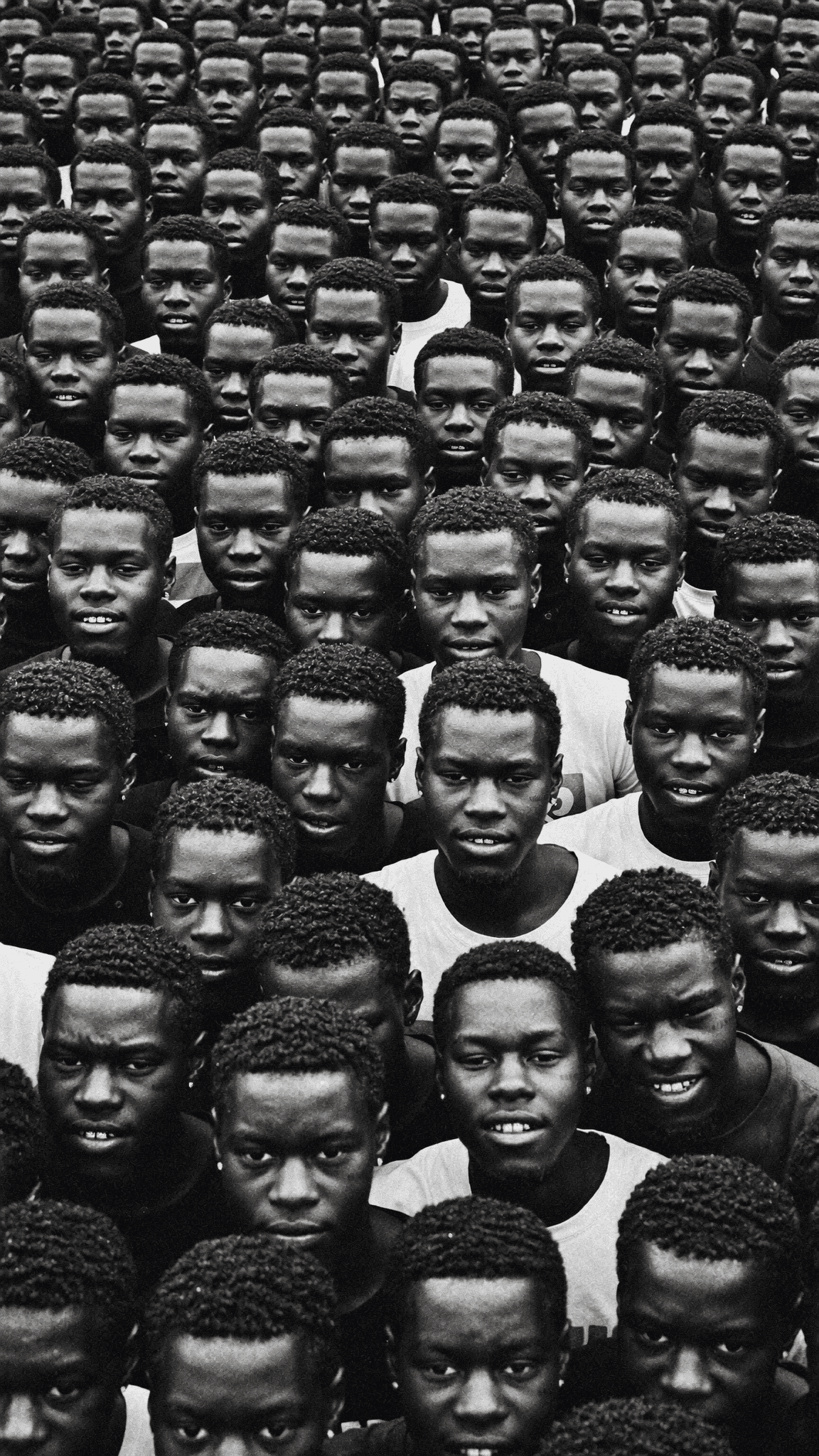 A large group of young men with similar hairstyles and expressions are closely packed together in a black-and-white photograph.