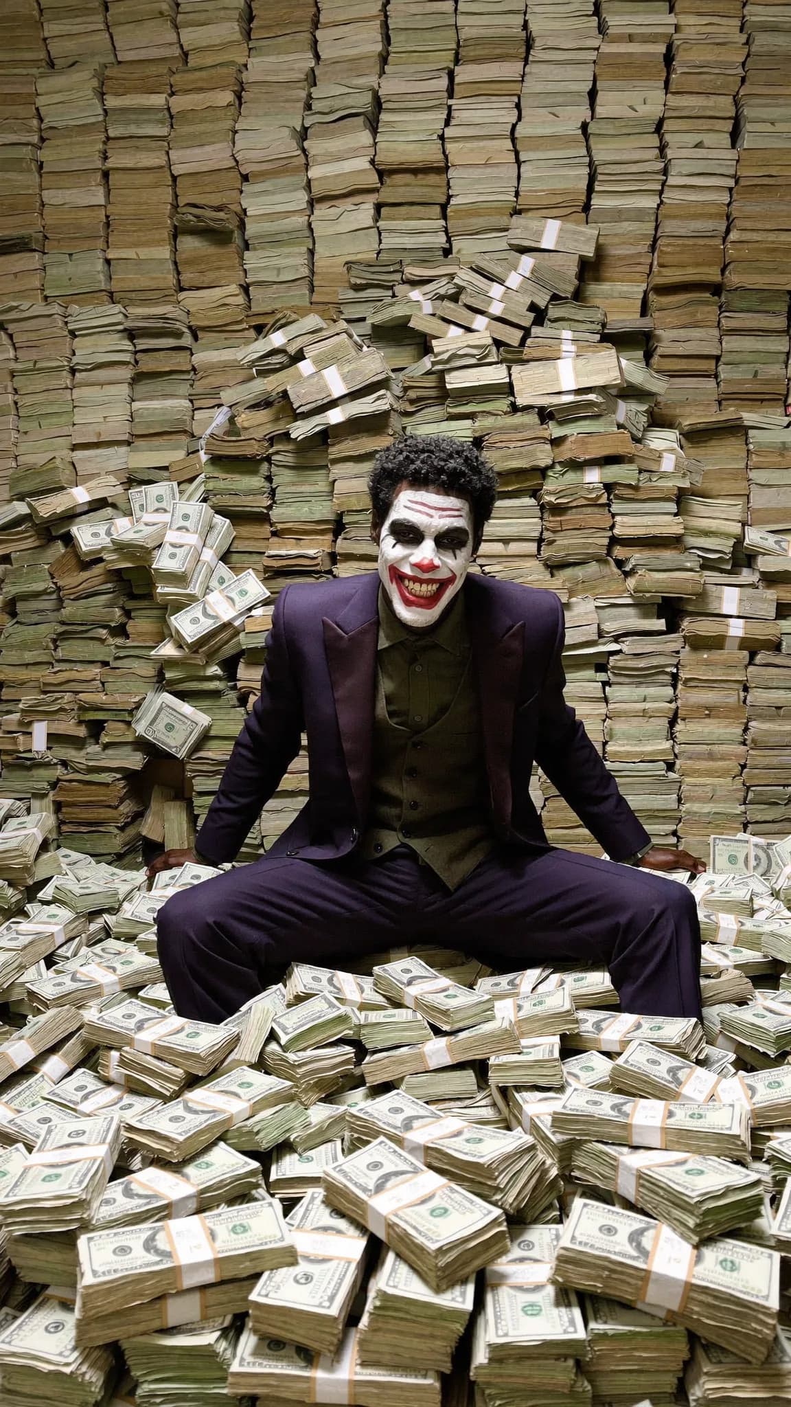 A person dressed in formal attire sits amidst a large pile of cash, with their face painted like The Joker.