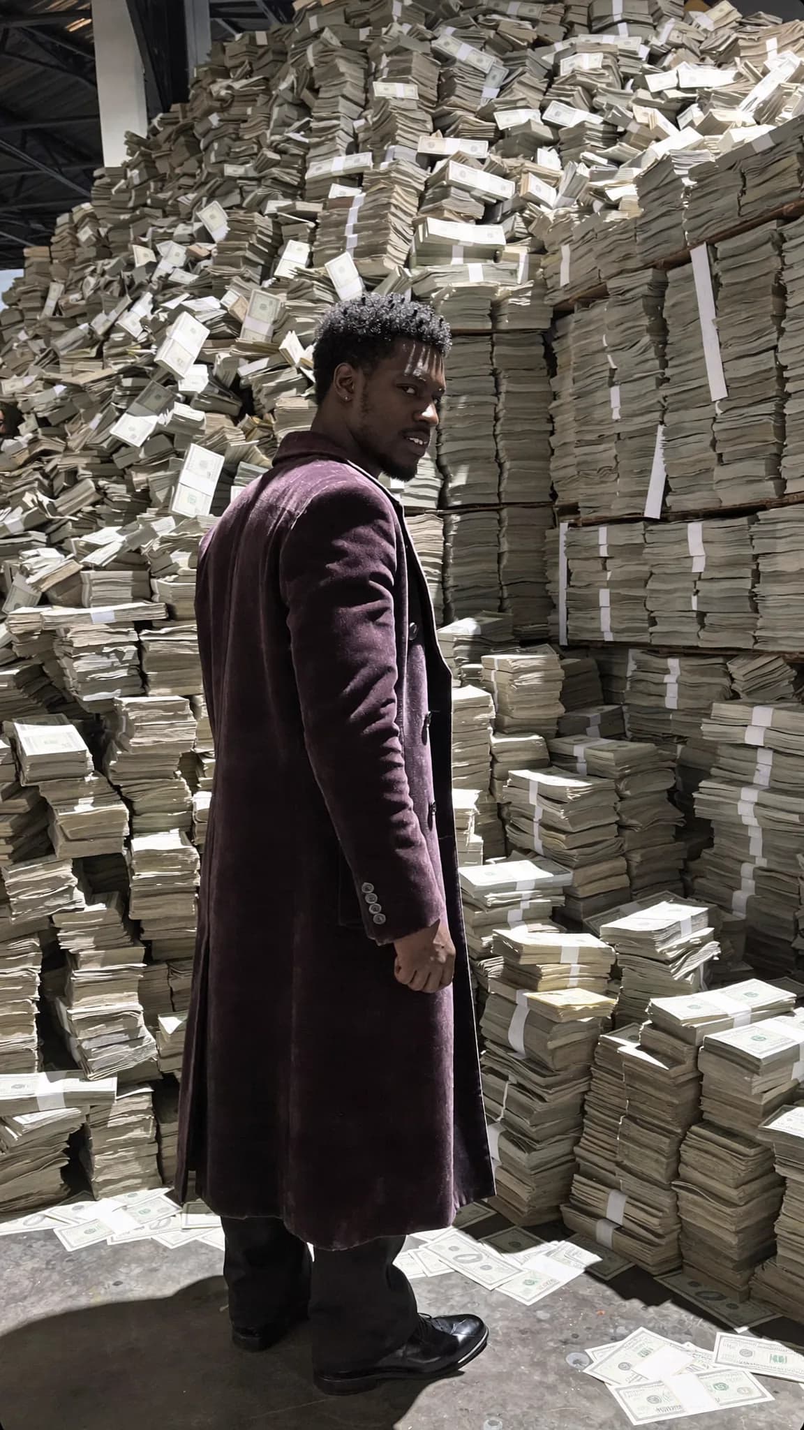 A man stands confidently in front of a large pile of cash, dressed in formal attire.