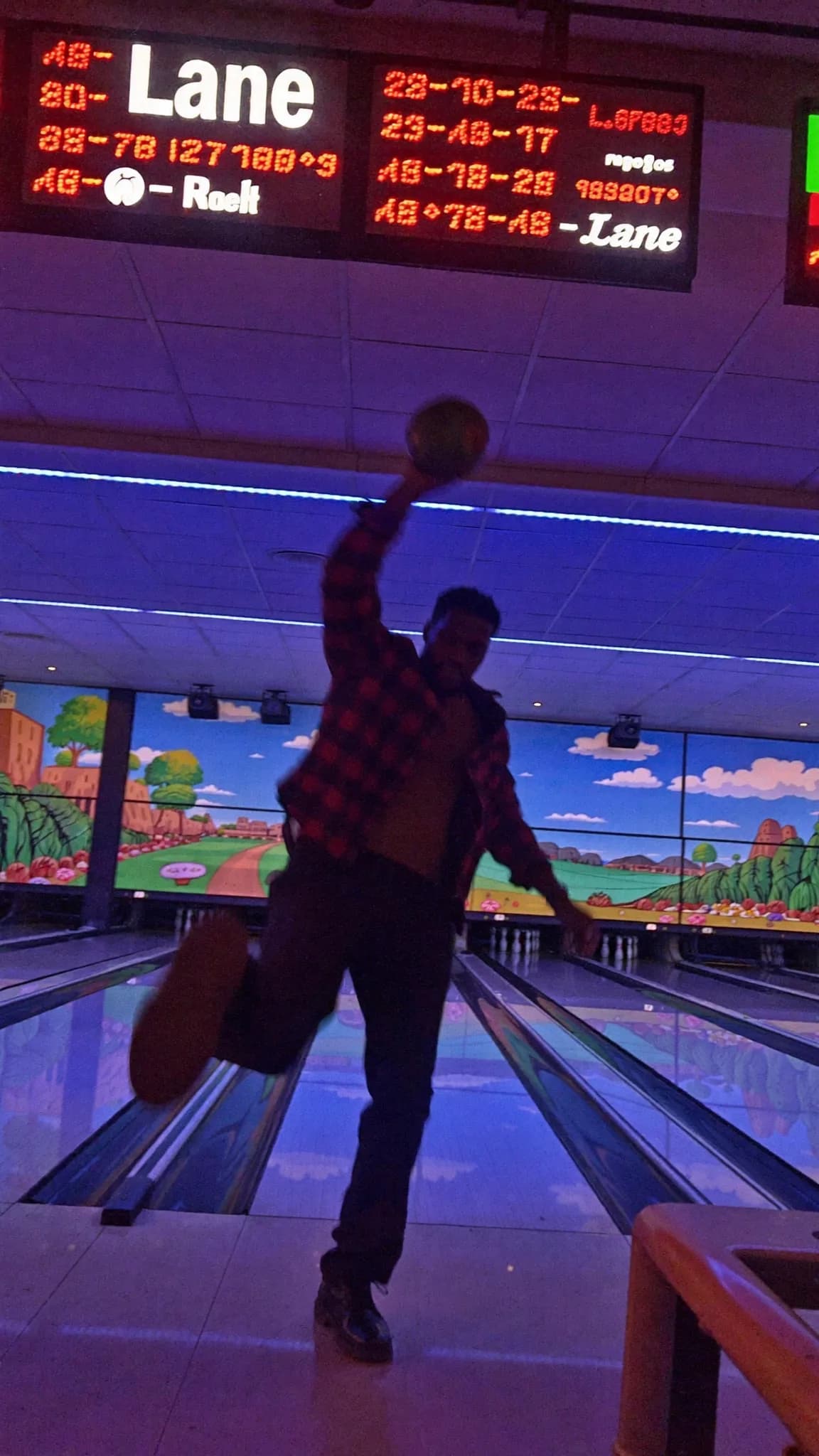 A person is bowling in a colorful alley with an action pose.