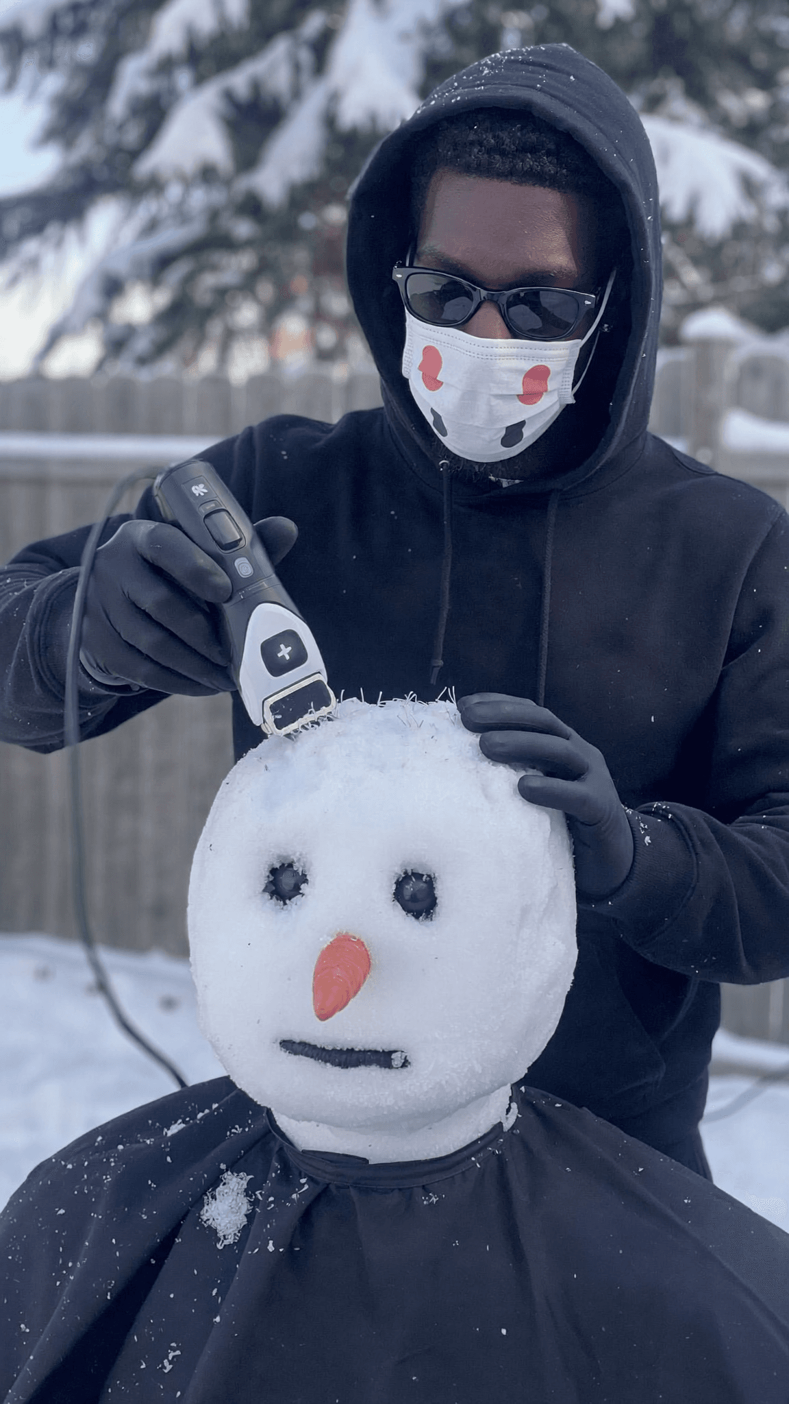 A person is grooming a snowman with an electric trimmer in a snowy outdoor setting.