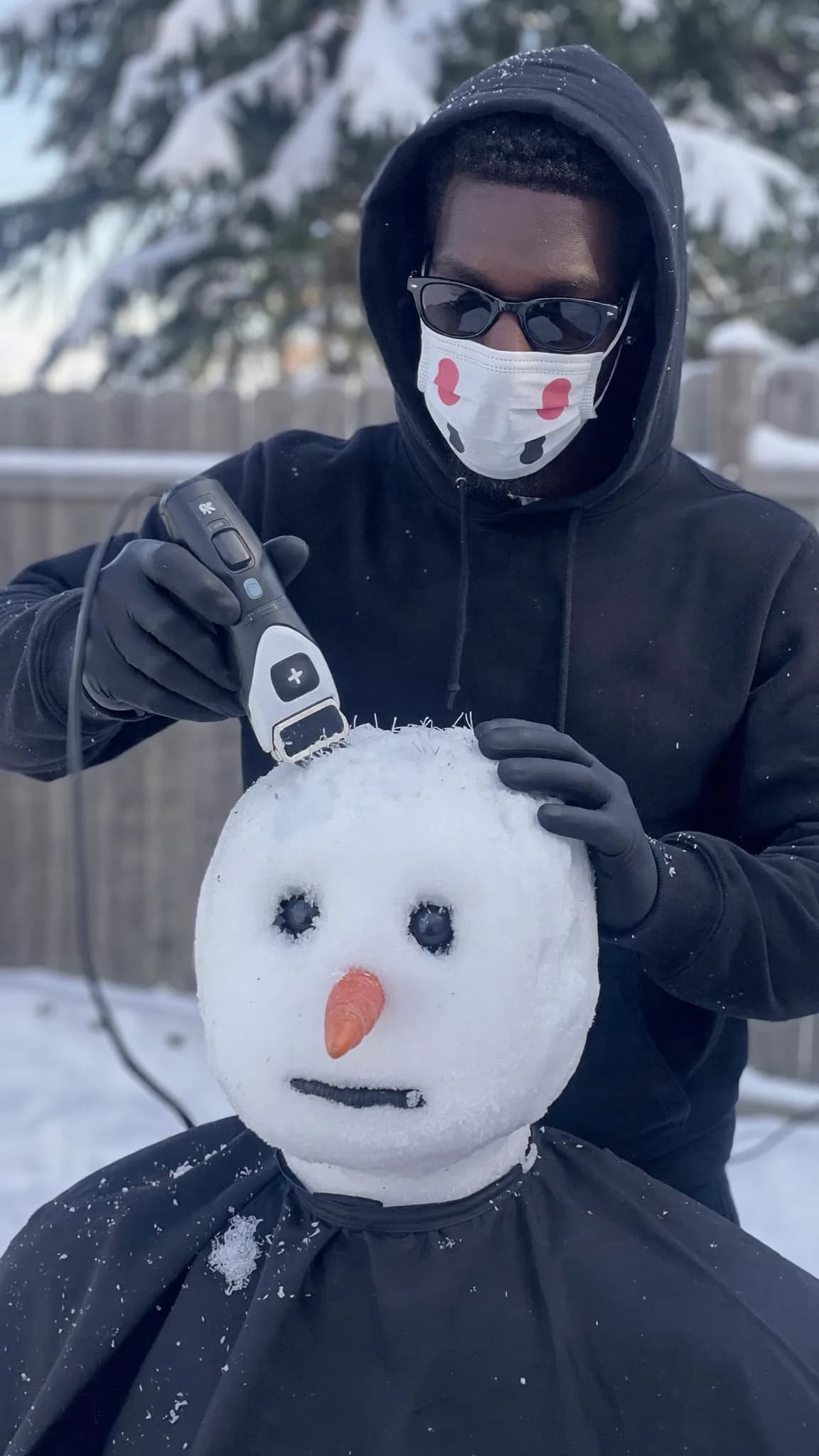 A person is grooming a snowman with an electric trimmer in a snowy outdoor setting.