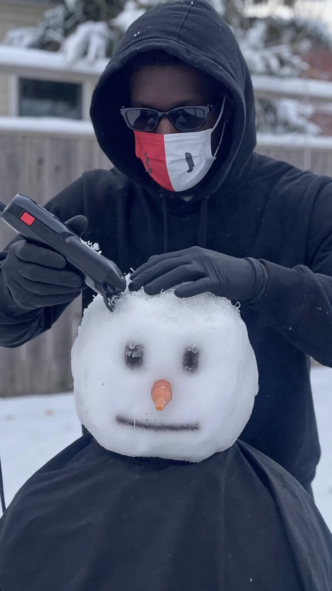 A person is grooming a snowman with an electric trimmer outdoors in the winter.