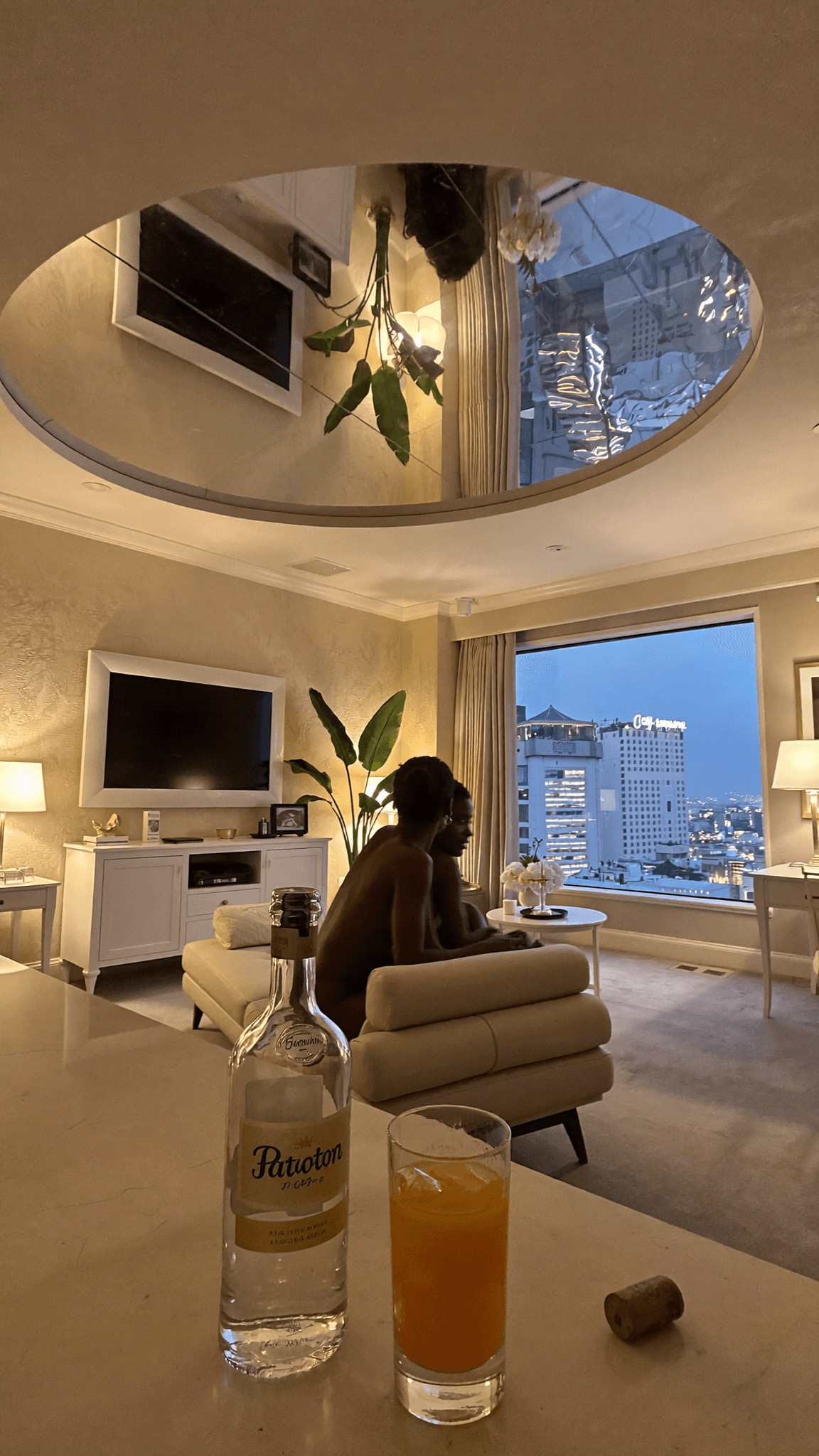 A person is seated in a bedroom with an intimate mood, enjoying a drink.