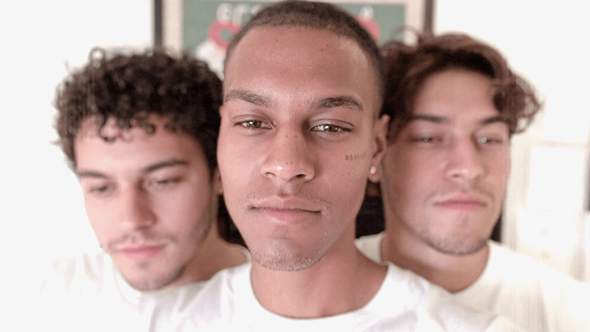 Three young men in casual attire pose closely together for a portrait.