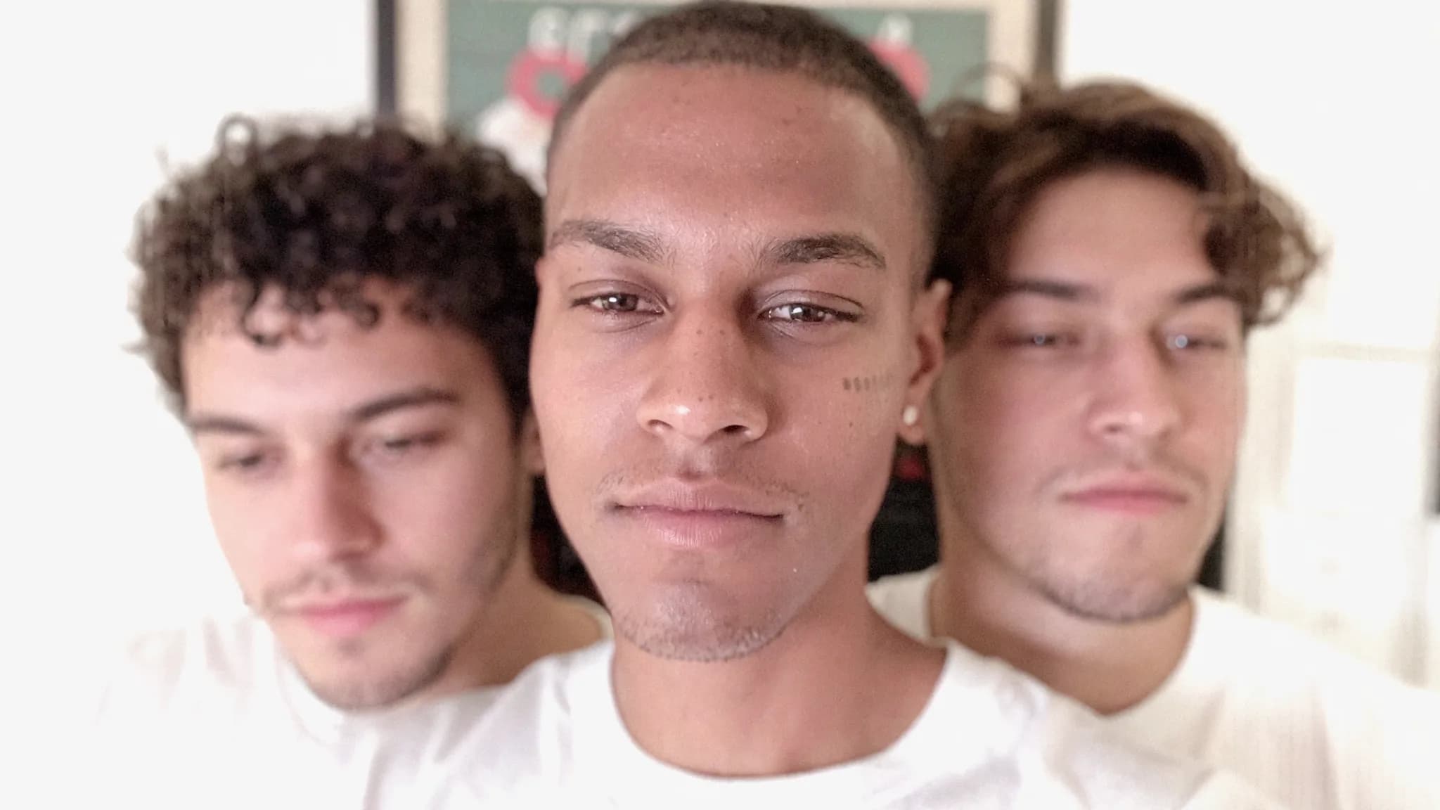 Three young men in casual attire pose closely together for a portrait.