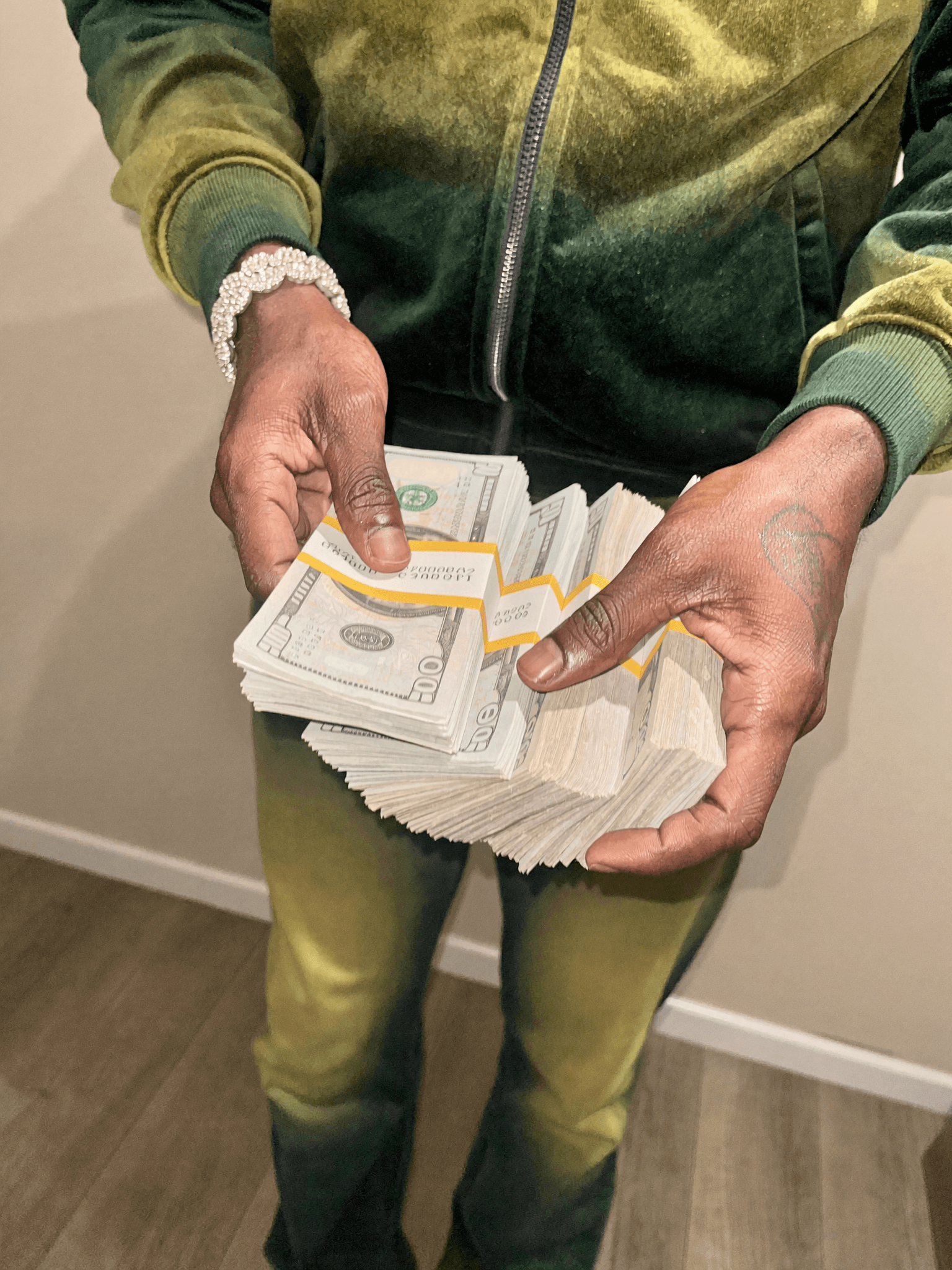 A person in casual athleisure holds a large stack of US dollar bills.