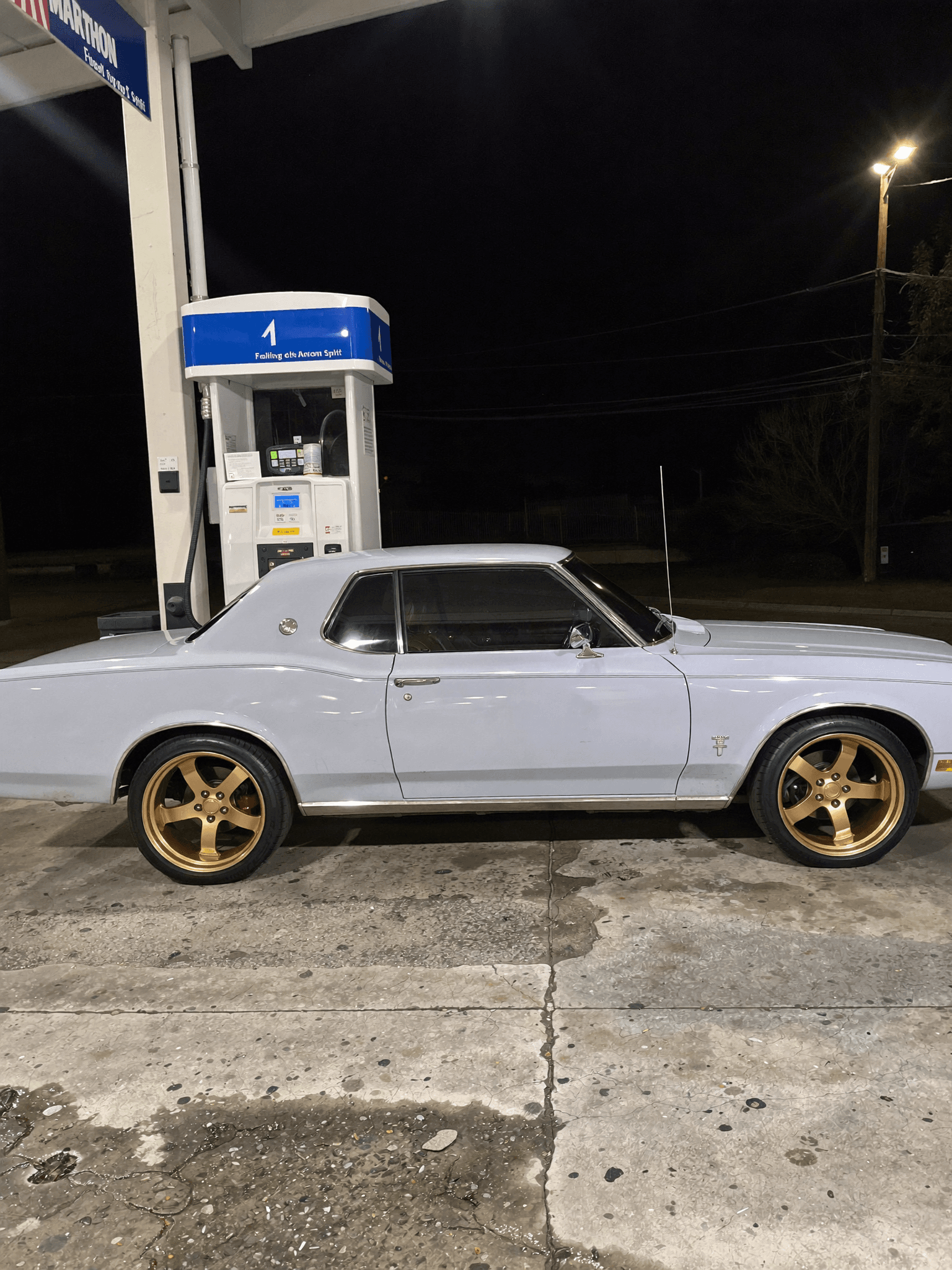 A classic car is parked at a gas station during nighttime.