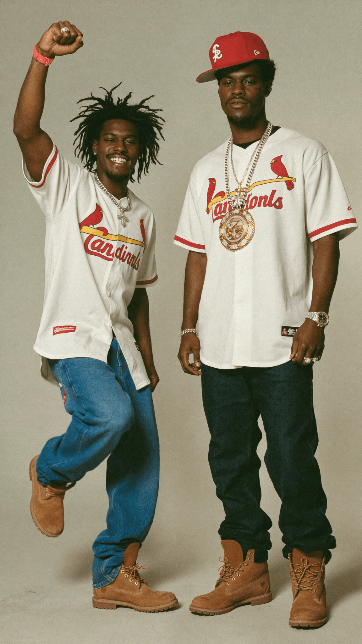 Two individuals in casual attire pose confidently, wearing Cardinals jerseys and Timberland boots.