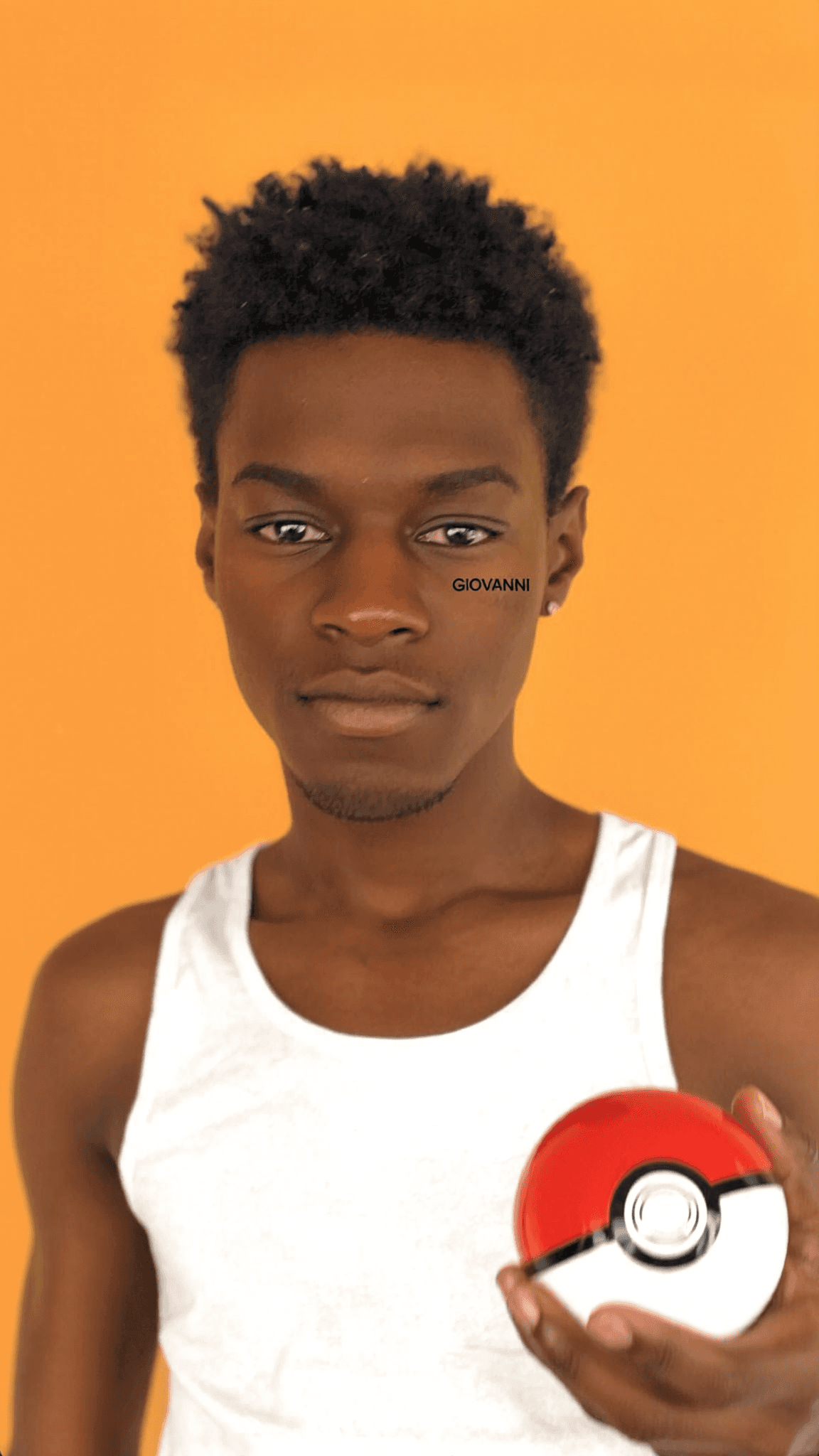A young man with a pixie cut holds a Poké Ball in front of an orange background.