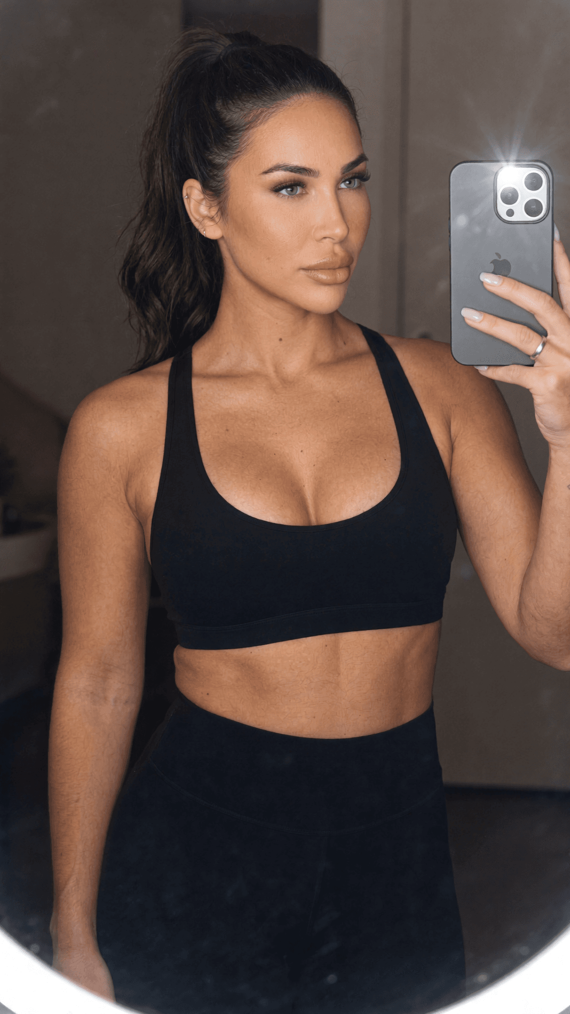 A woman in black athleisure poses for a mirror selfie.