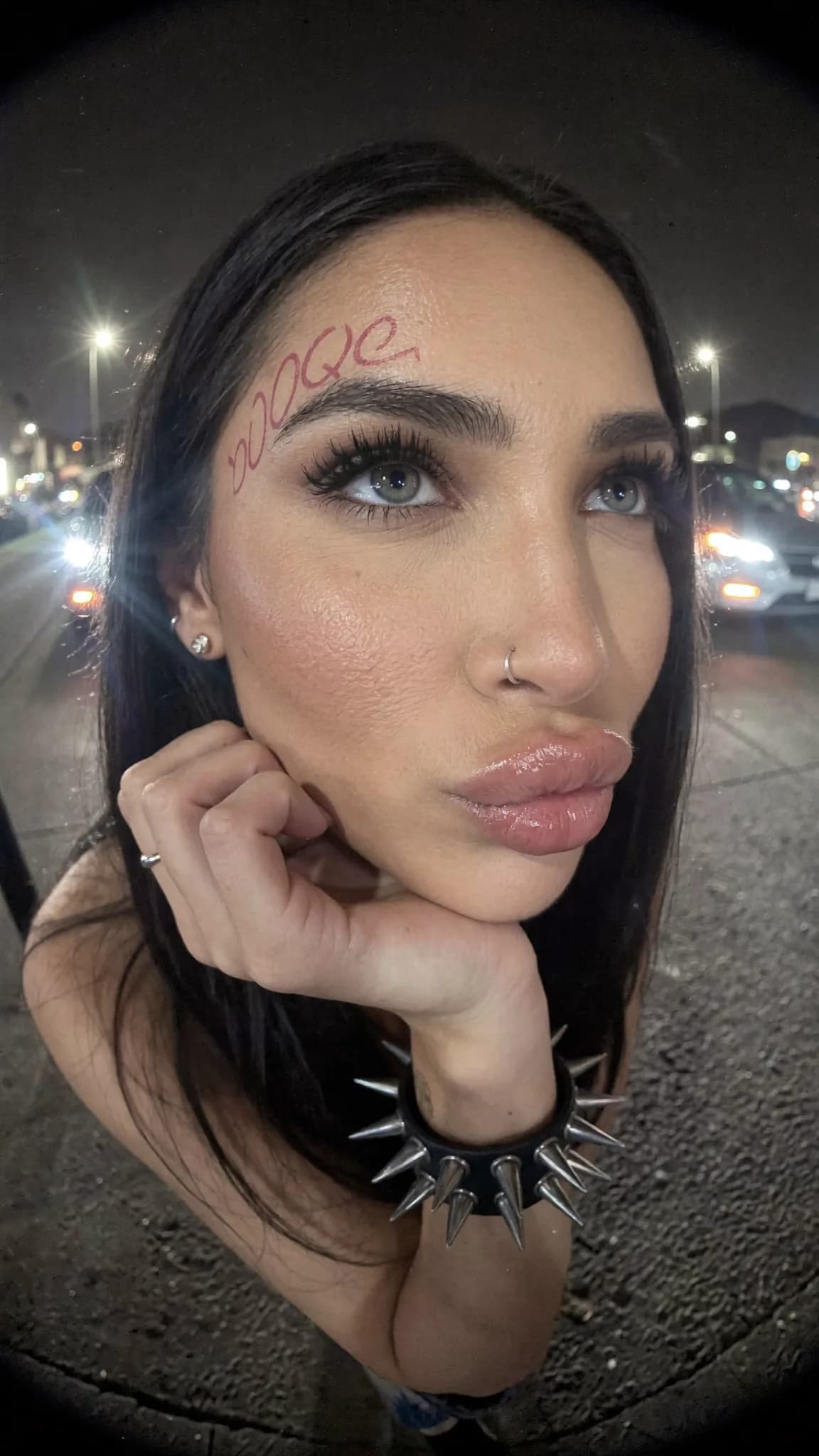 A woman with a septum ring and beauty mark poses for the camera at night.