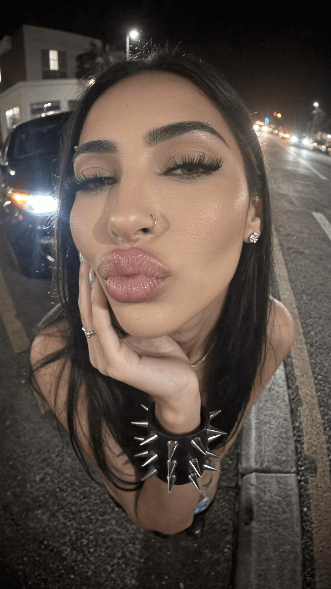A woman with a septum ring and spiked bracelet poses on the street at night.