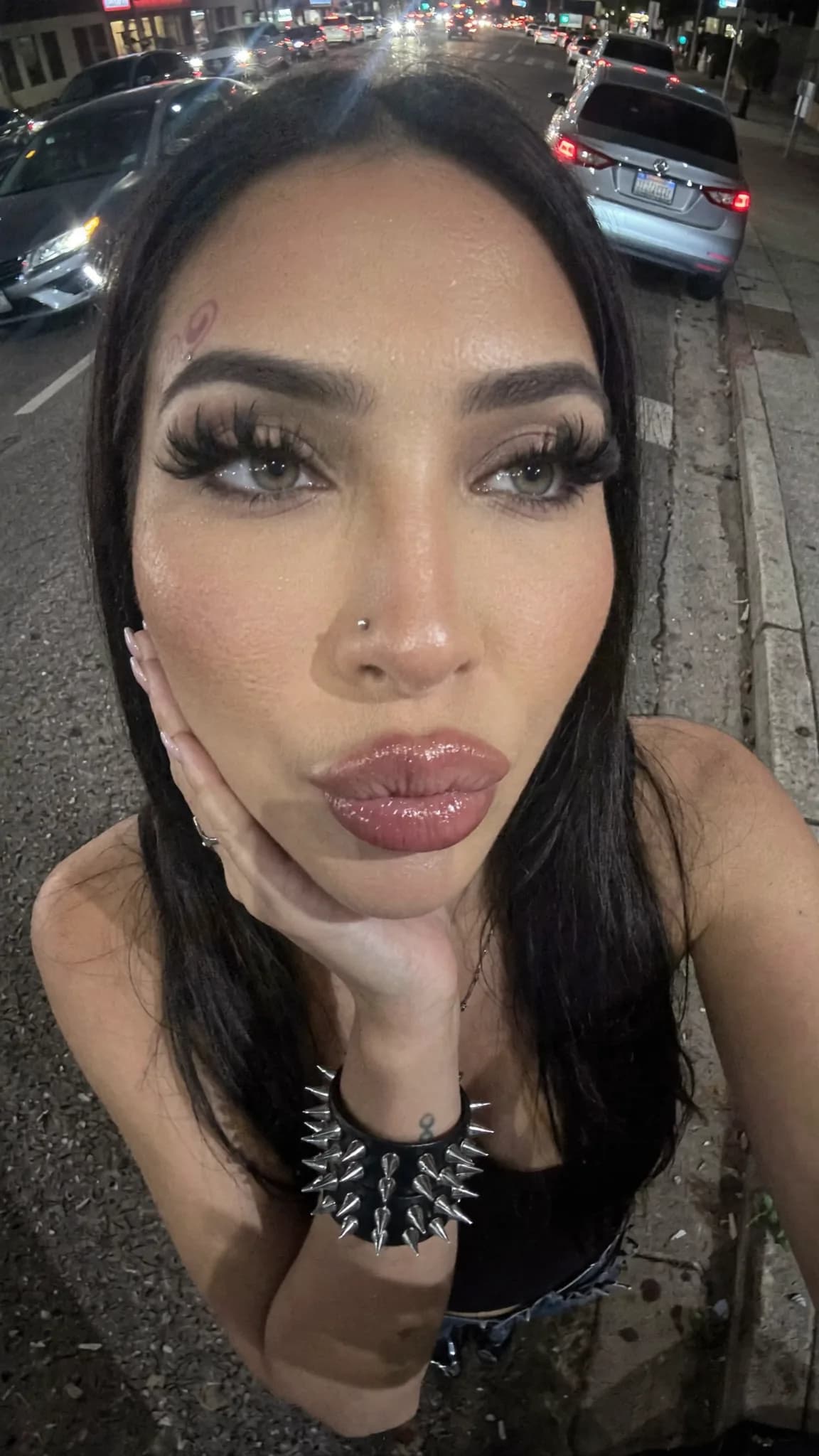 A woman with a septum ring and beauty mark poses on the street at night.