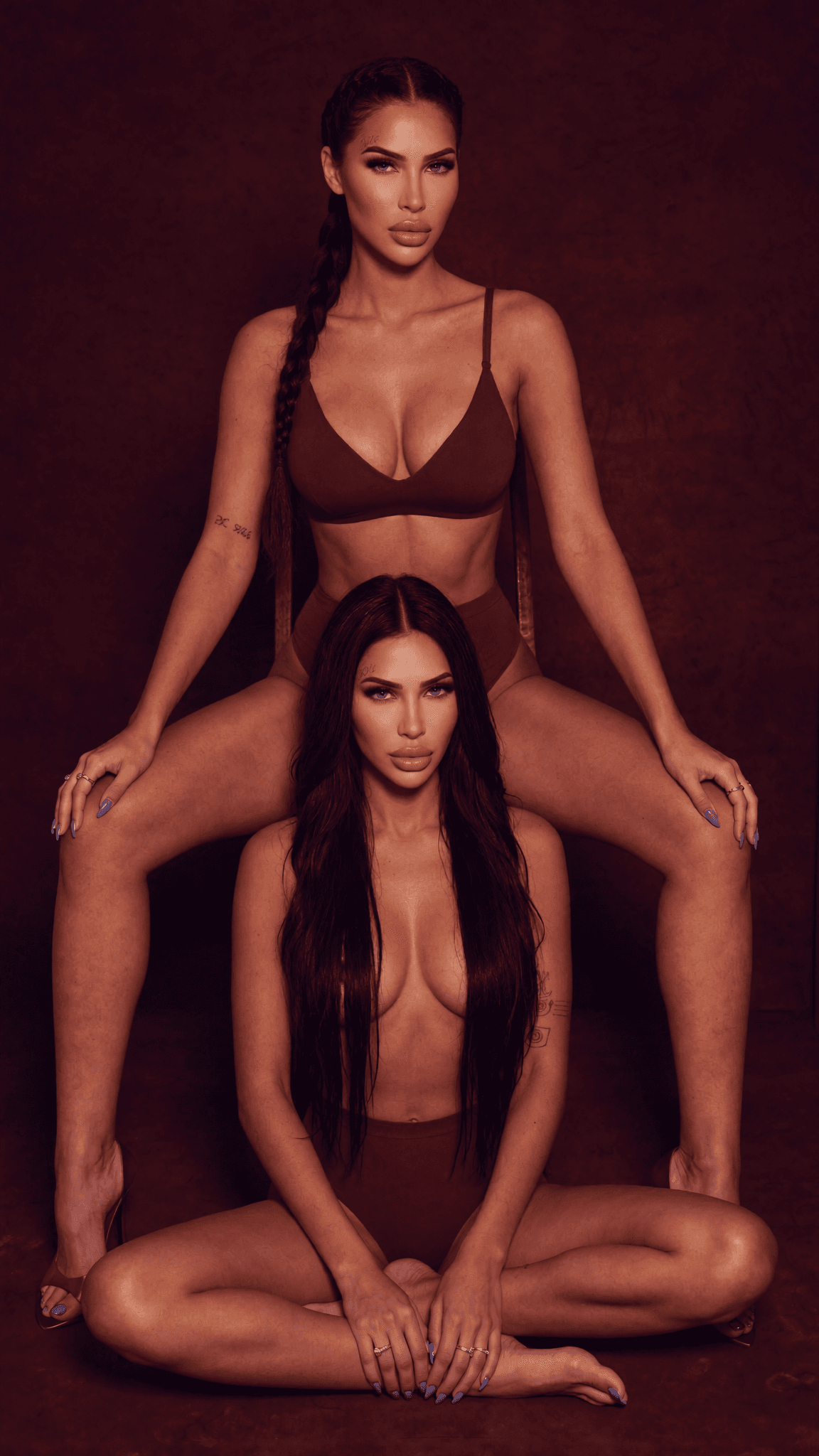 Two women in lingerie pose intimately against a studio backdrop.