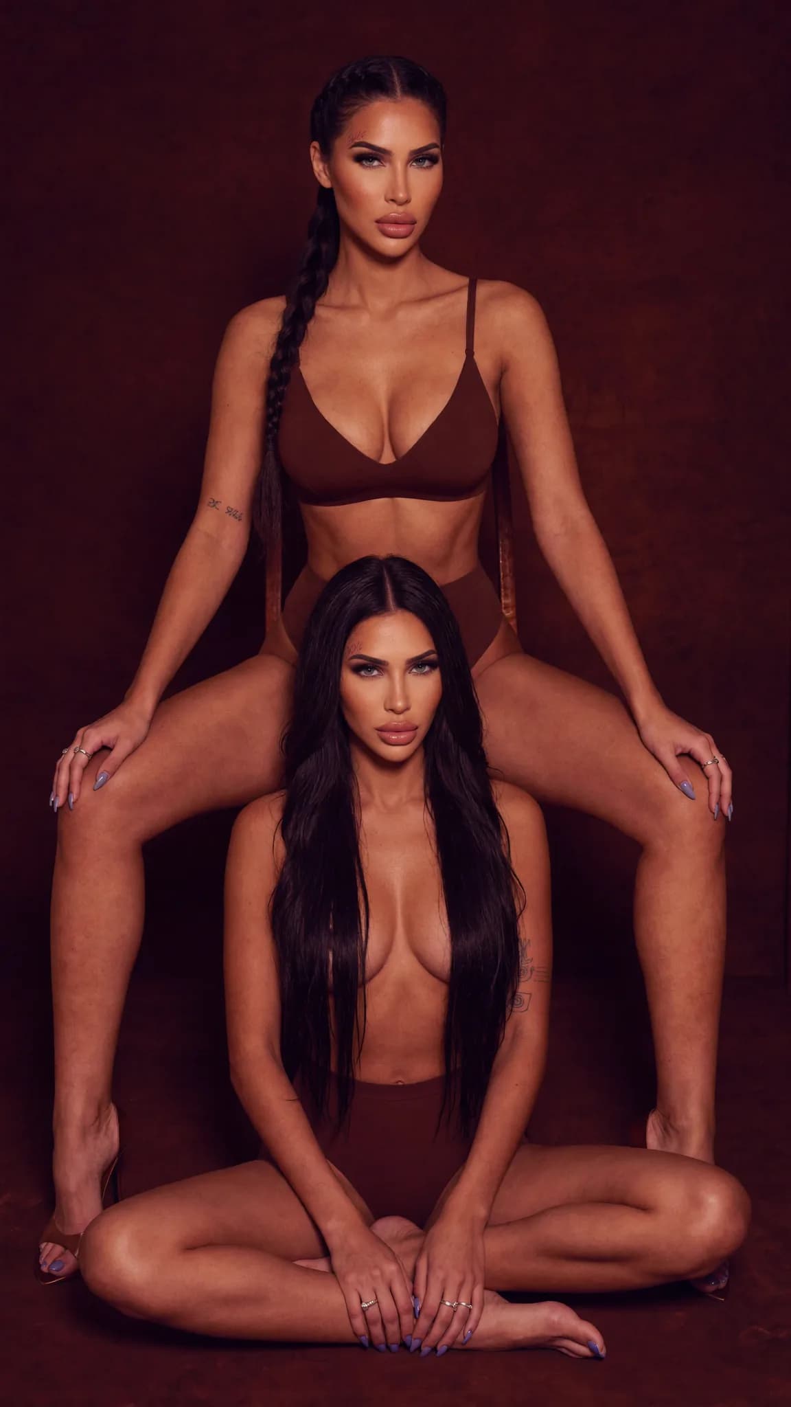 Two women in lingerie pose intimately against a studio backdrop.