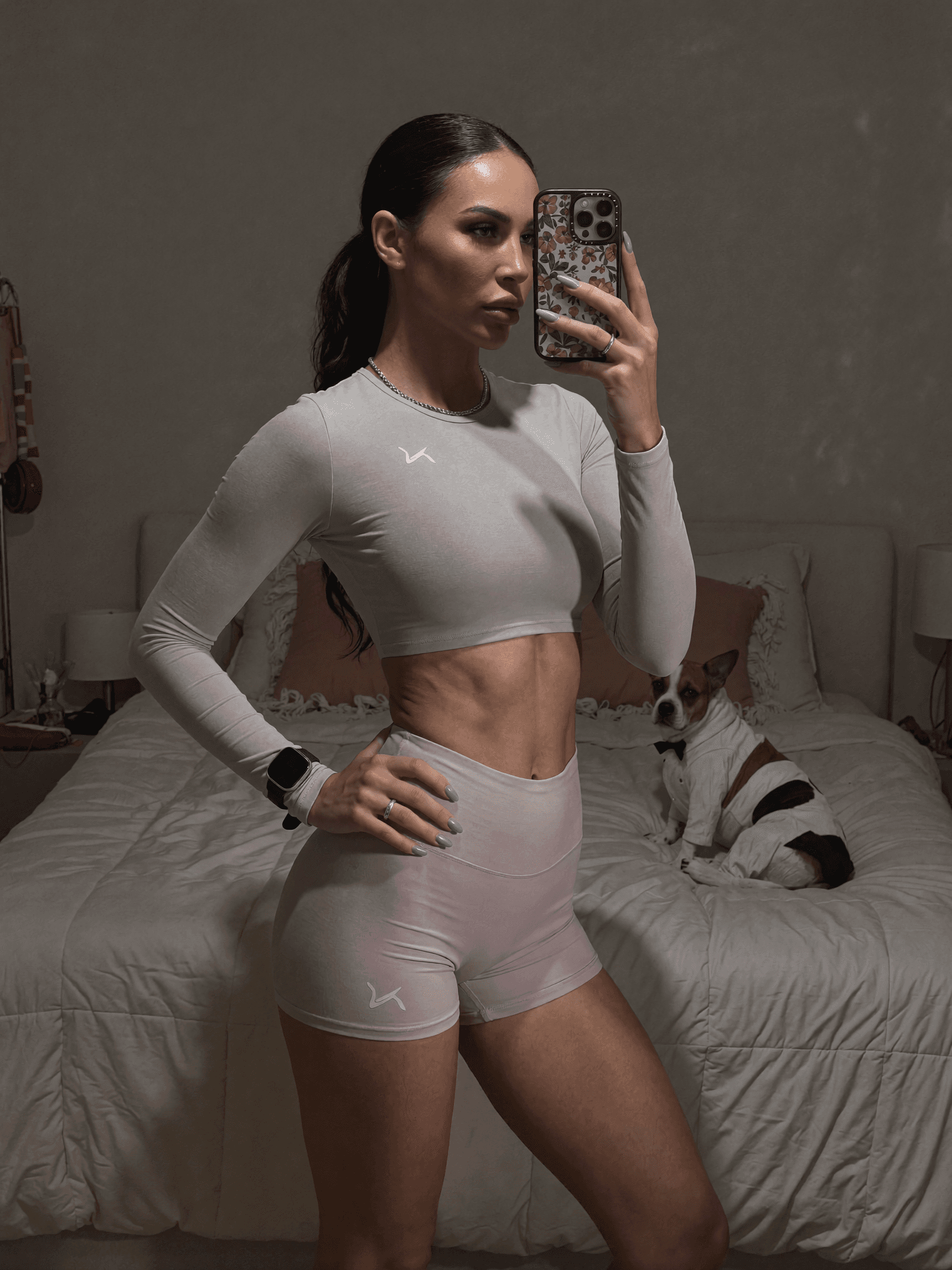 A woman in athletic wear poses confidently in a bedroom with her dog.