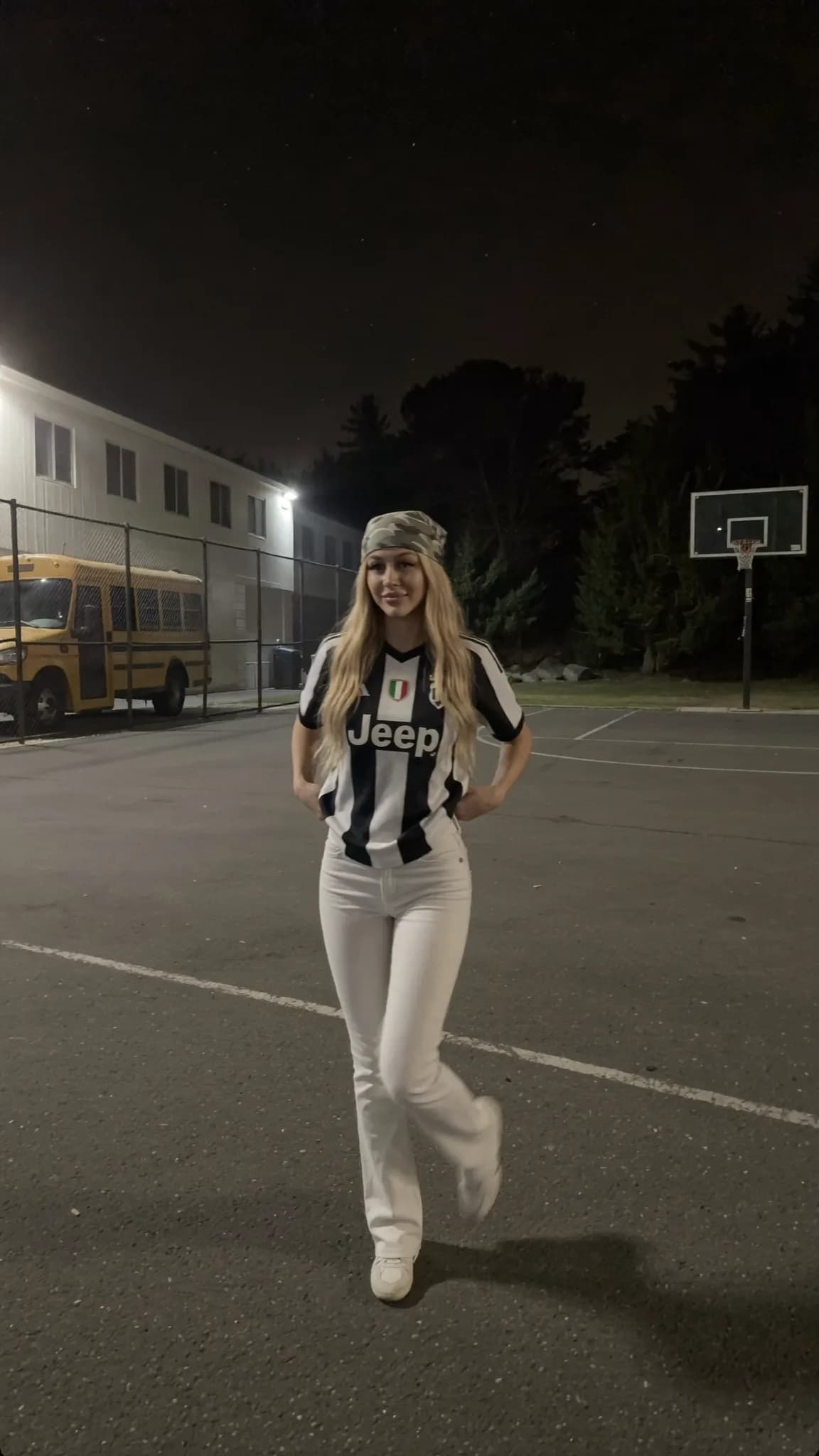 A woman in a Corvette Blondie outfit poses confidently on an outdoor basketball court at night.