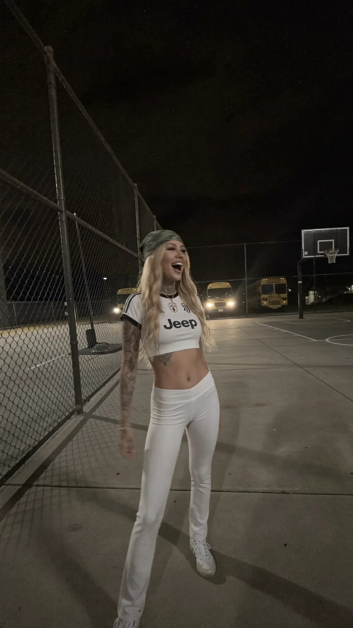 A woman in a crop top and leggings stands confidently on an outdoor basketball court at night.