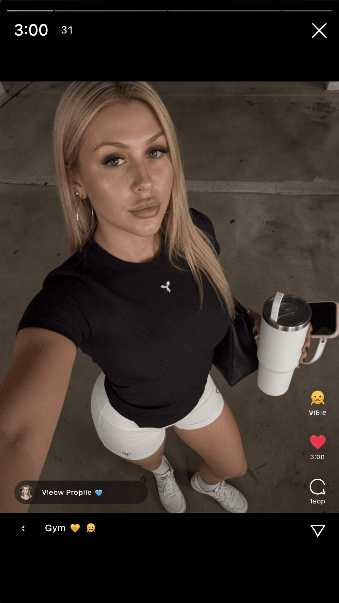 A woman in athletic attire poses for a selfie outdoors, holding a tumbler and phone.