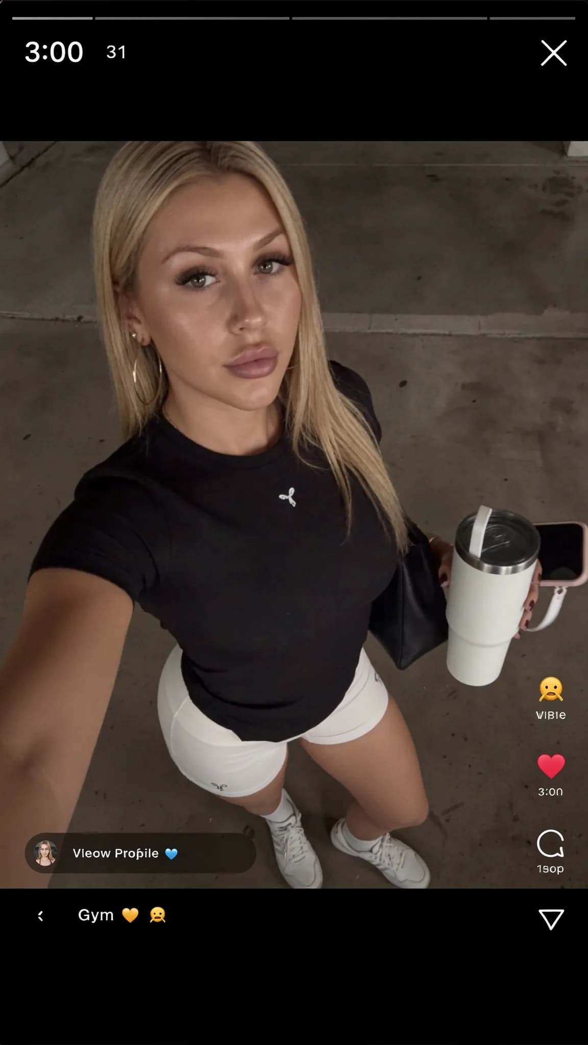 A woman in athletic attire poses for a selfie outdoors, holding a tumbler and phone.