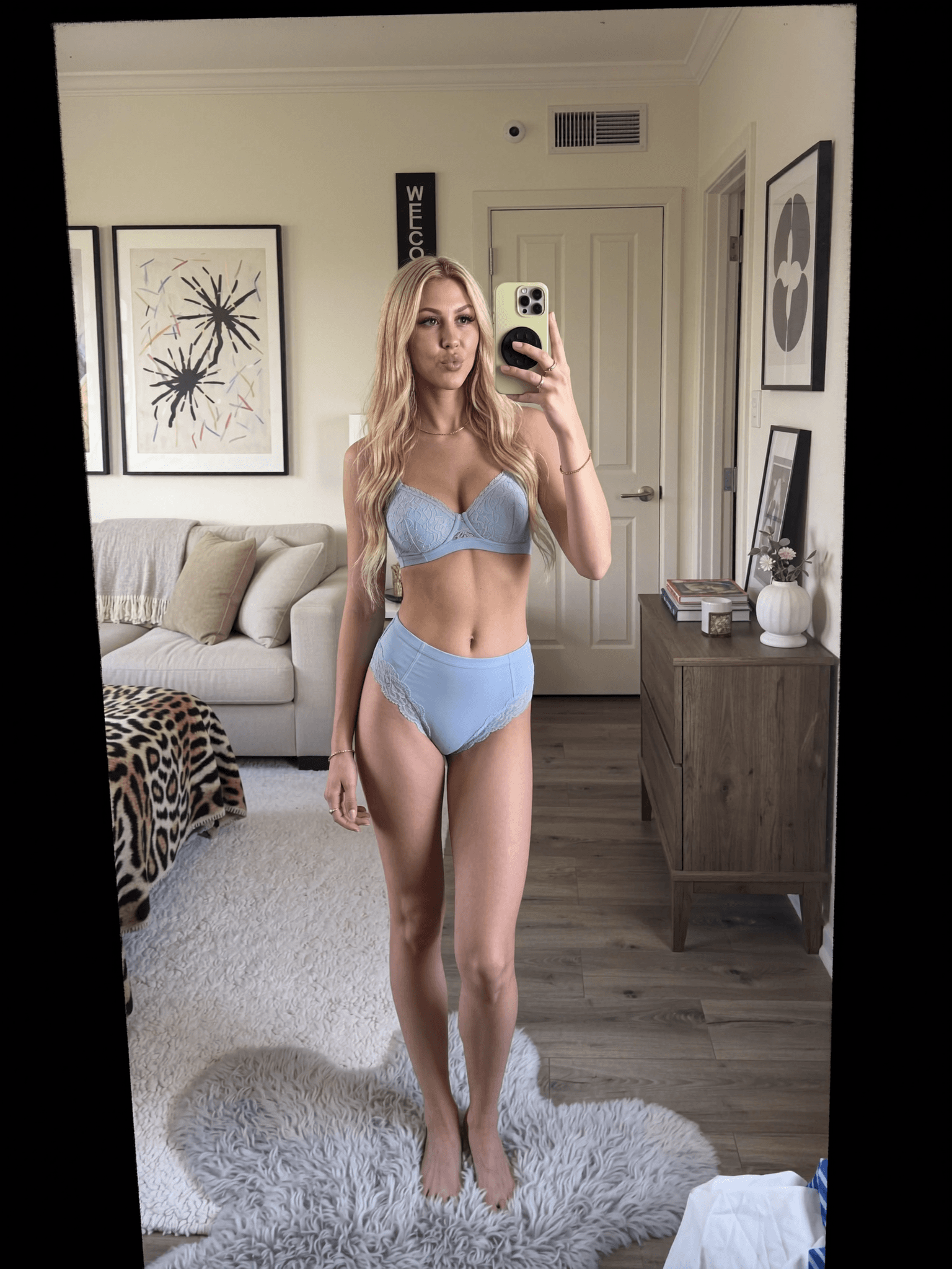 A woman in lingerie poses confidently in a bedroom setting.